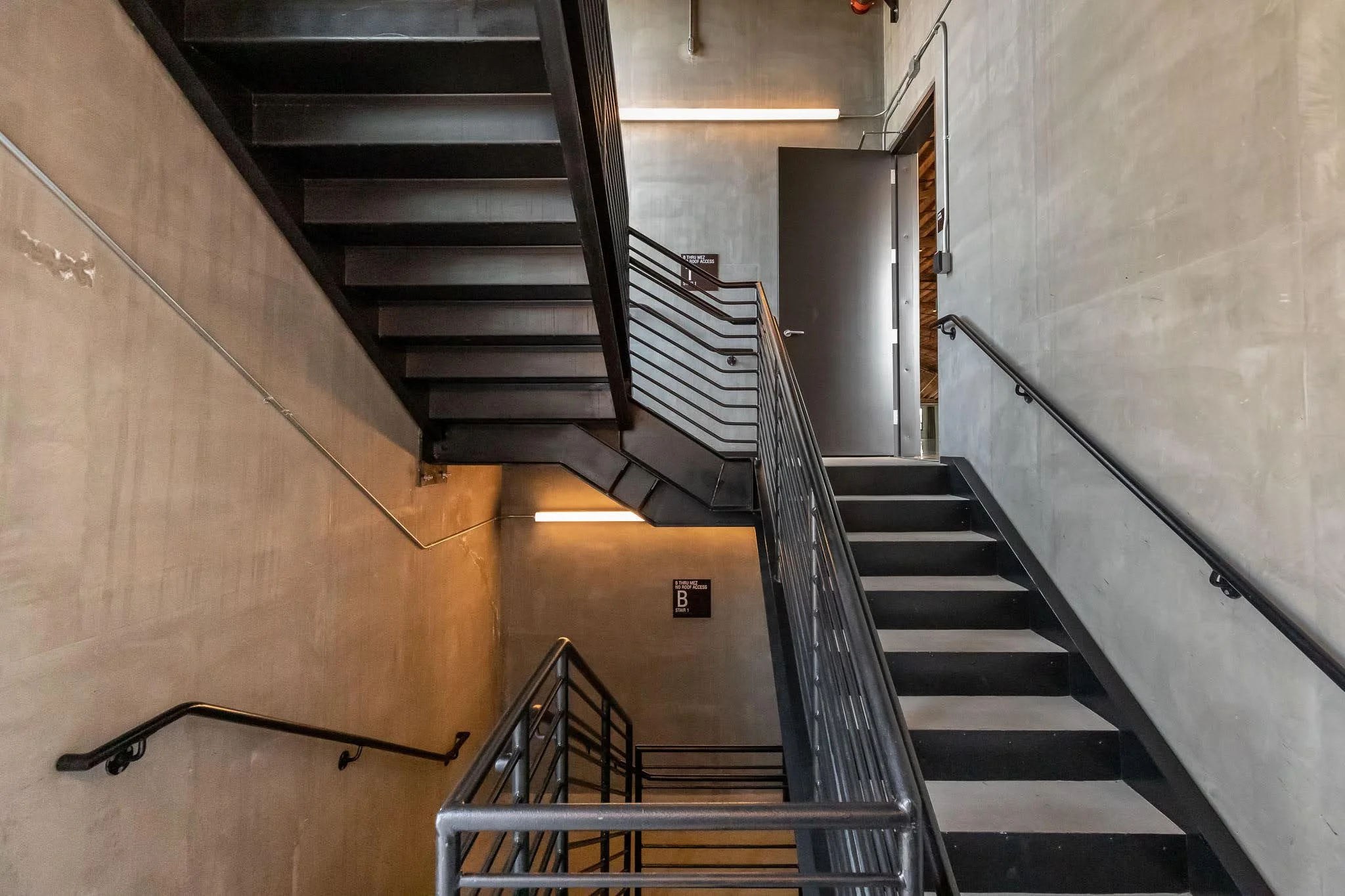 Interior view of a modern, industrial-style staircase with black metal railings and concrete walls in a building.