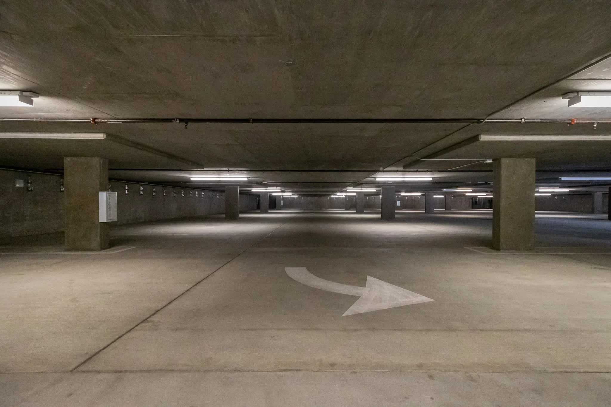 Underground parking garage with a white arrow painted on the concrete floor, indicating a left turn.