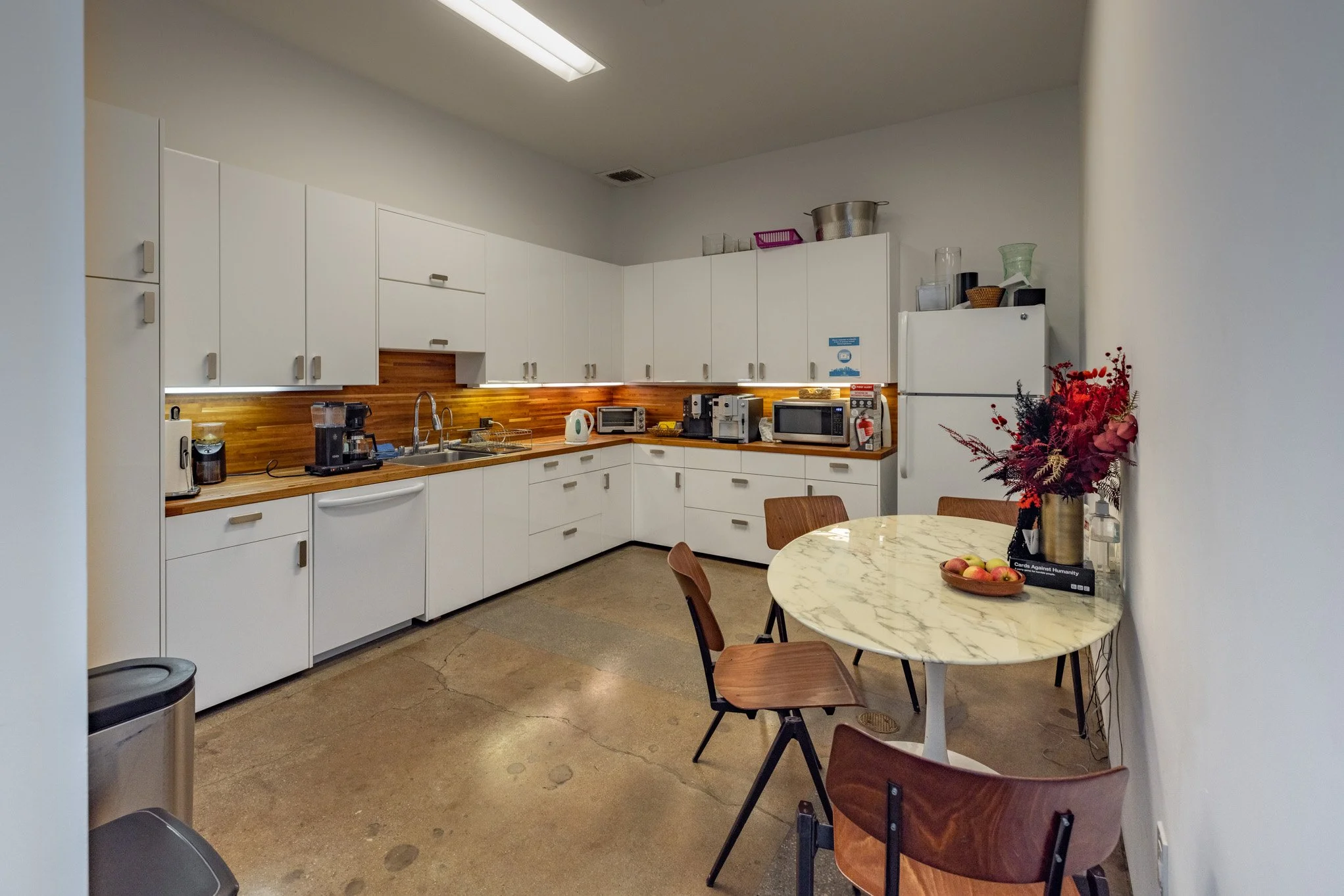 Kitchen with white cabinets, wooden countertops, a white refrigerator, a marble round table with wooden chairs, and various appliances including a coffee maker, microwave, and toaster.