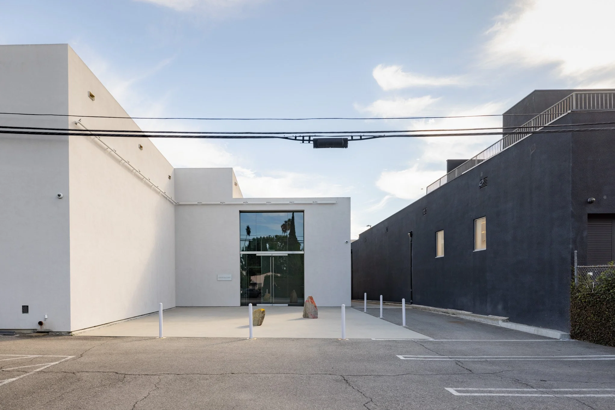Modern white and black building with large glass door, small windows, and parking lot in front.