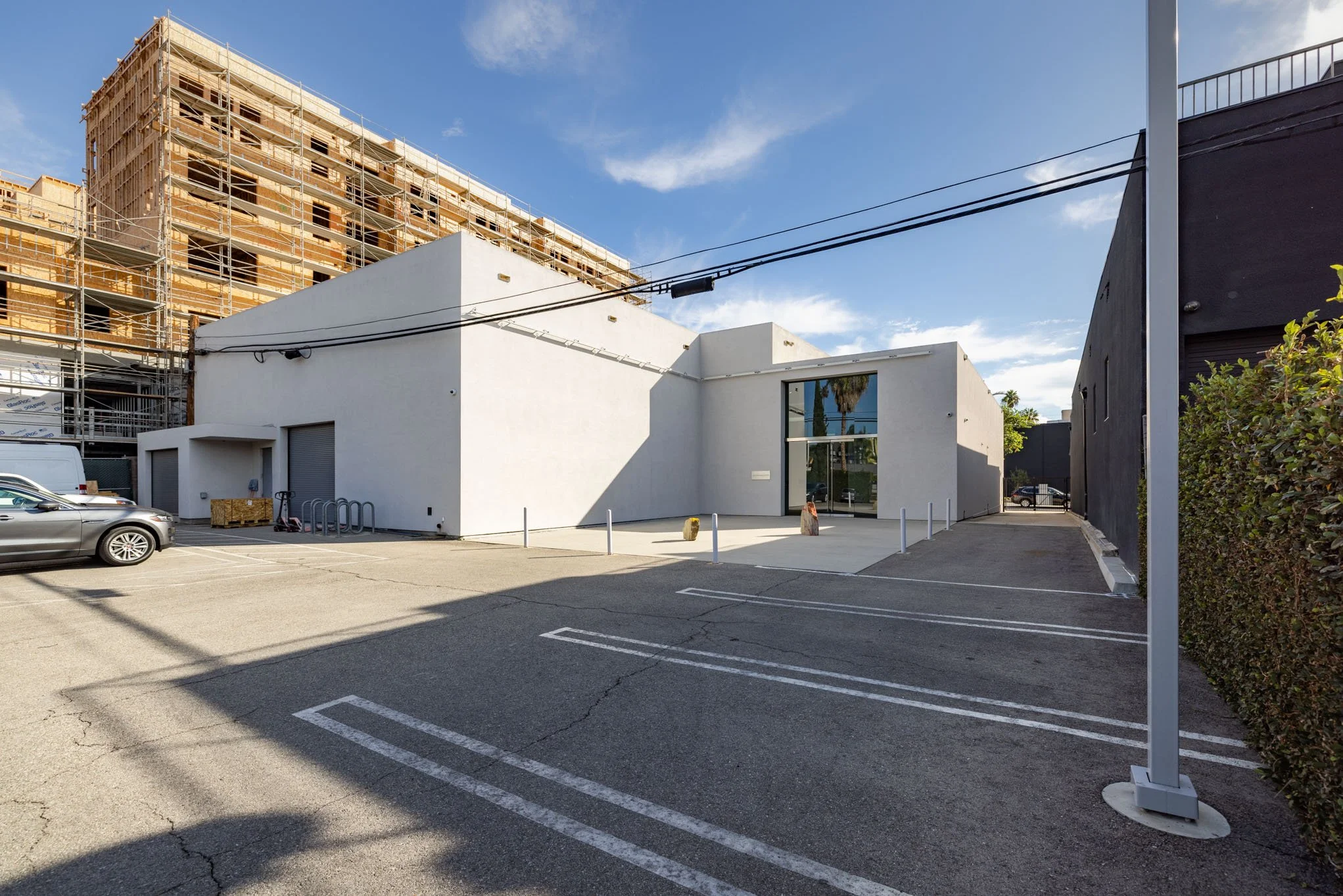 Empty parking lot with a white modern building, a black building, and a construction site with scaffolding in the background, under a clear blue sky.