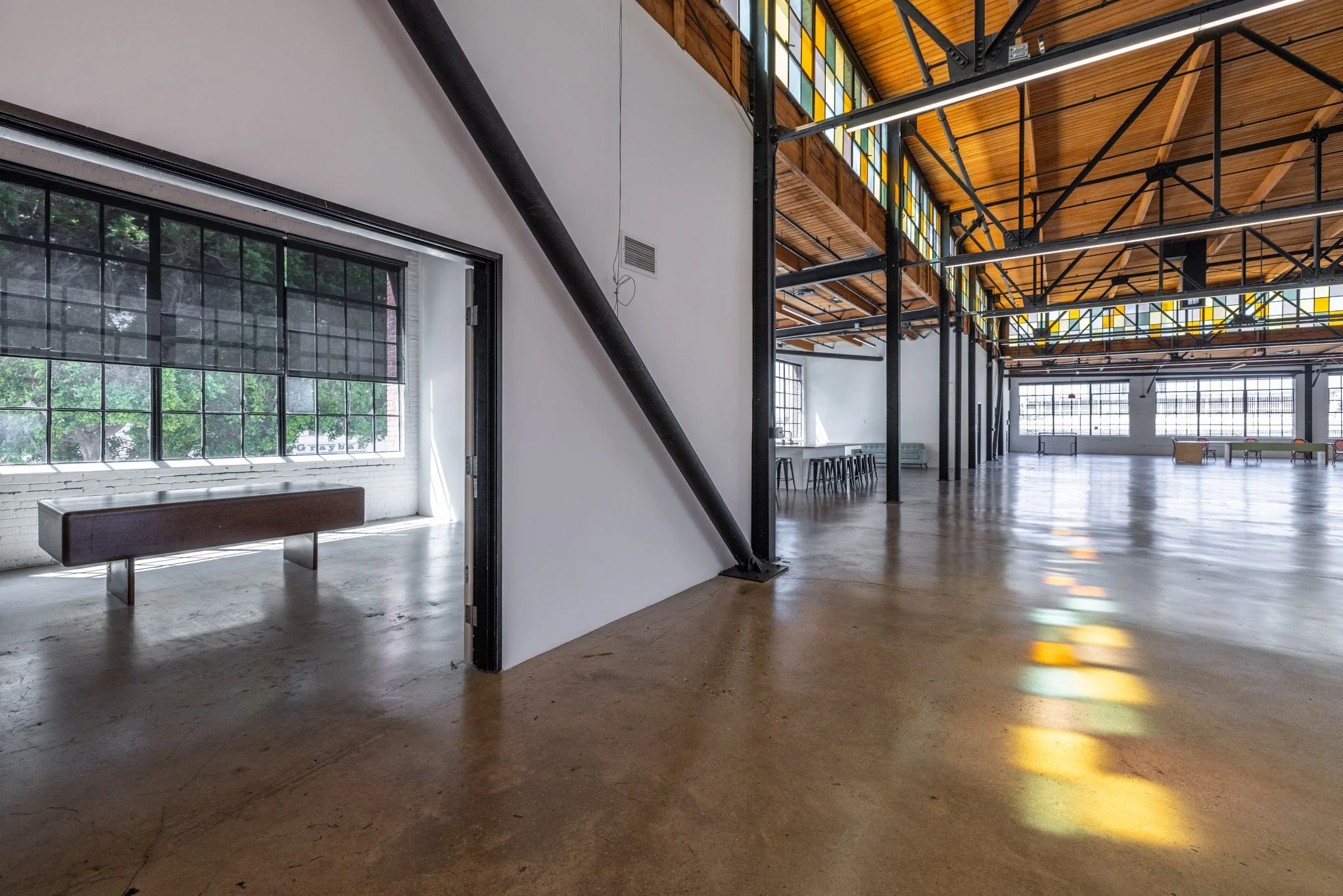 Spacious industrial-style interior with large windows, stained glass accents, polished concrete floor, white walls, black steel support beams, and wooden ceiling.
