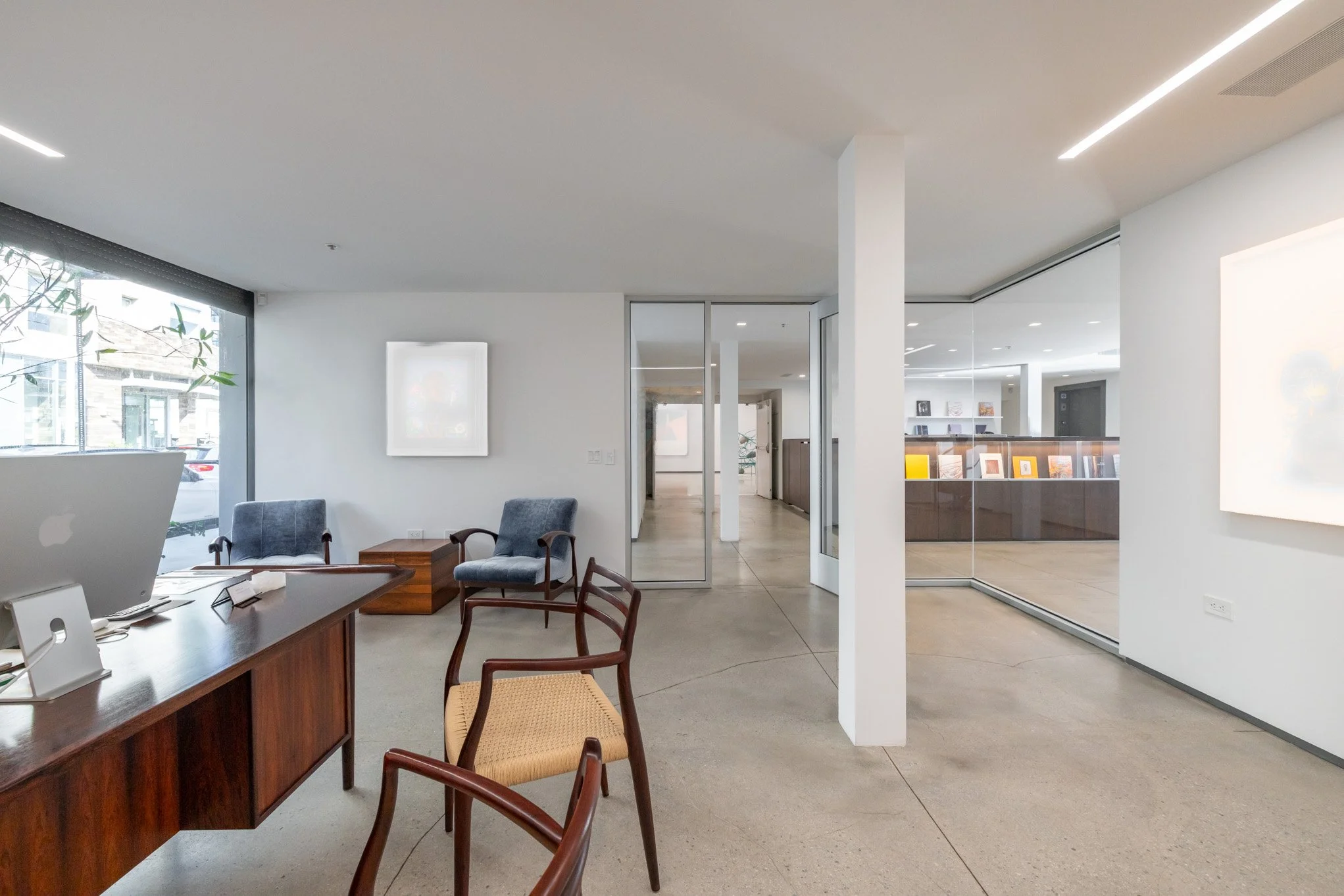 Modern office space with minimalist design, large windows, seating area, and a reception area with framed artwork and magazines.