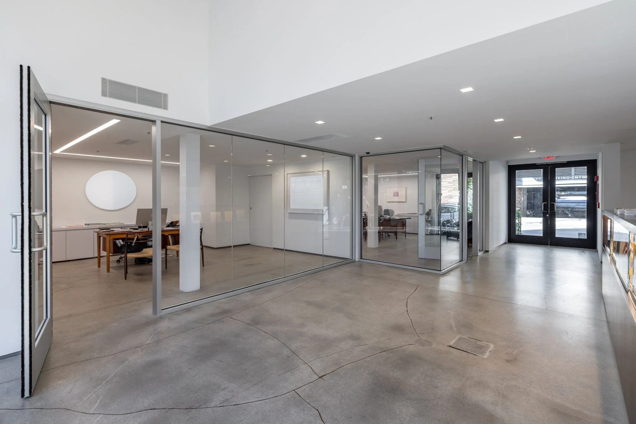Empty modern office space with glass walls, a glass door, and a view into separate rooms with desks and chairs.