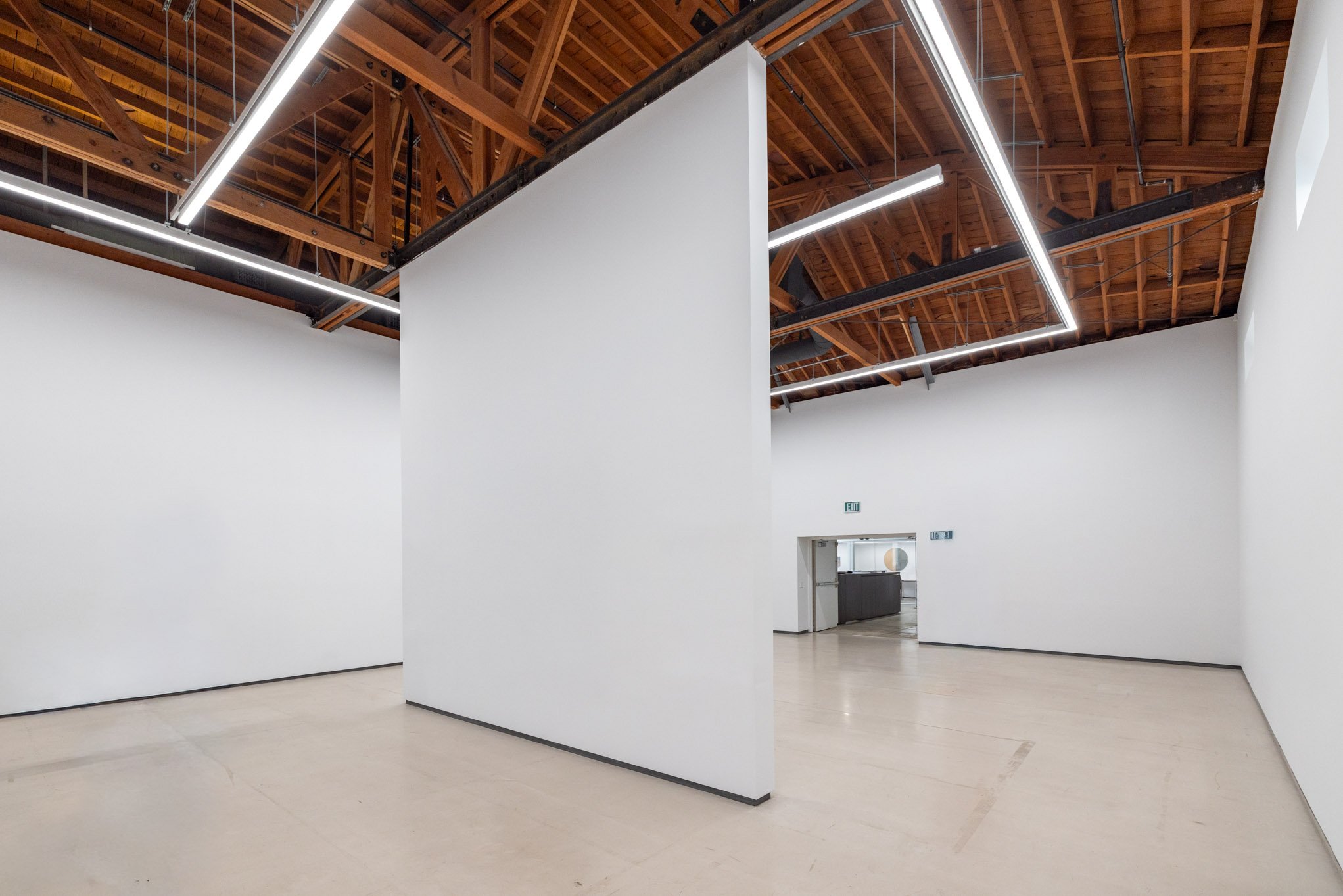 Empty modern art gallery with white walls, wooden ceiling with exposed beams, and LED light fixtures.