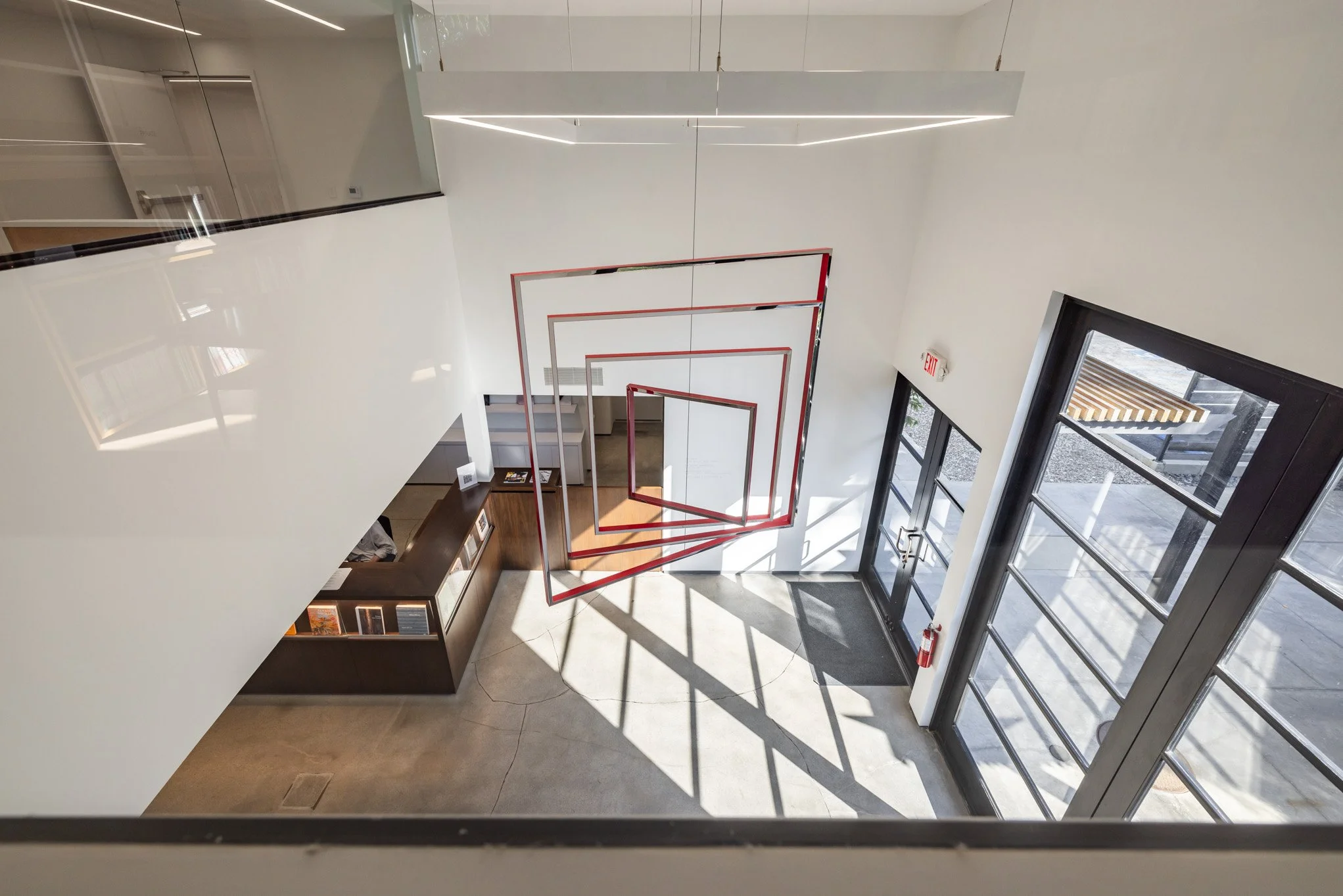 Interior view of a modern building entrance with oversized glass doors, a spiral red metal sculpture hanging from the ceiling, and a reception desk on the left.