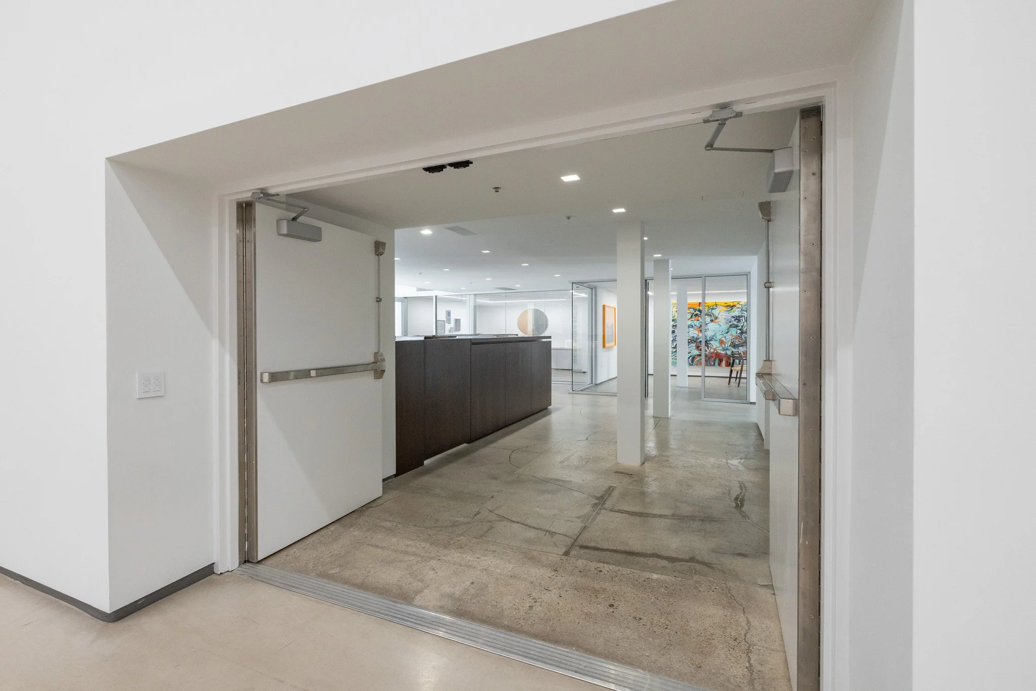 An open sliding door reveals a modern interior with artwork, bright lighting, and minimalist decor.