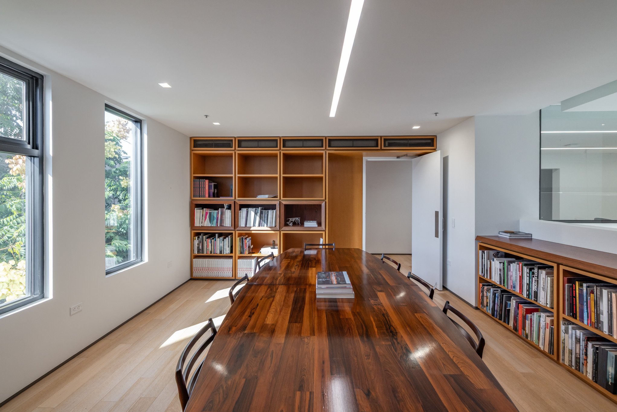 Modern conference room with a large wooden table, bookshelves, and windows with natural light.