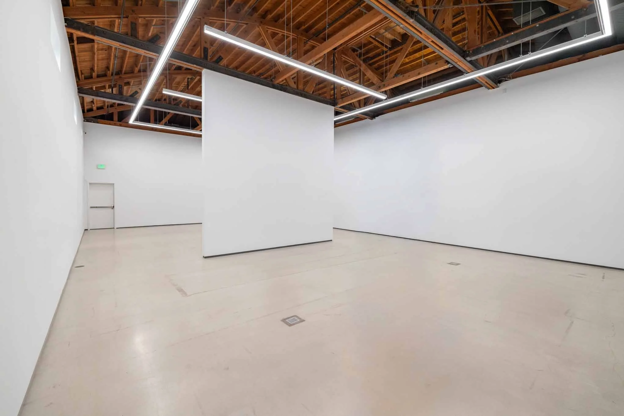 Empty art gallery with white walls, wooden ceiling, and modern lighting fixtures.