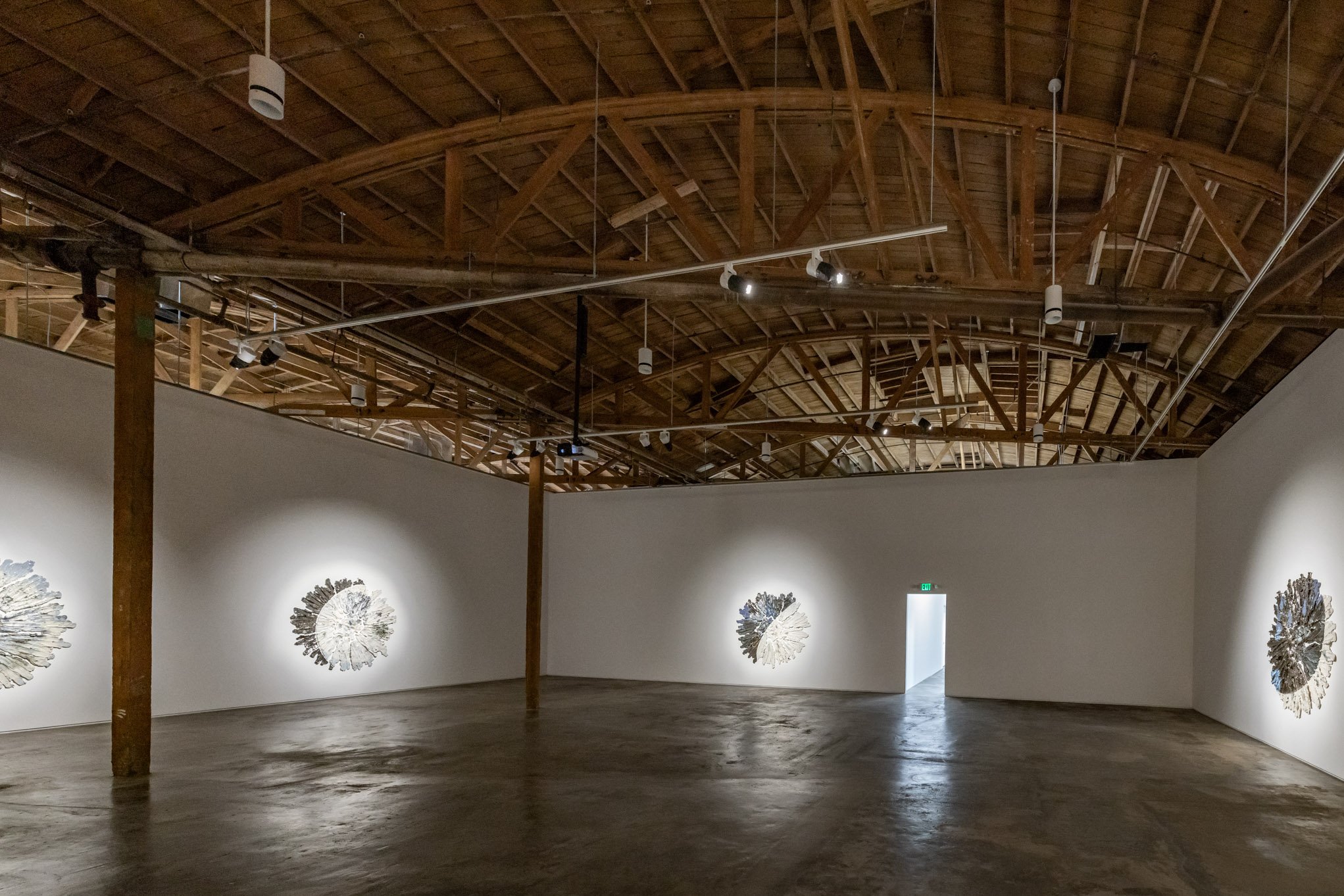 Art gallery with wooden ceiling, white walls displaying sculptures, and polished concrete floor.