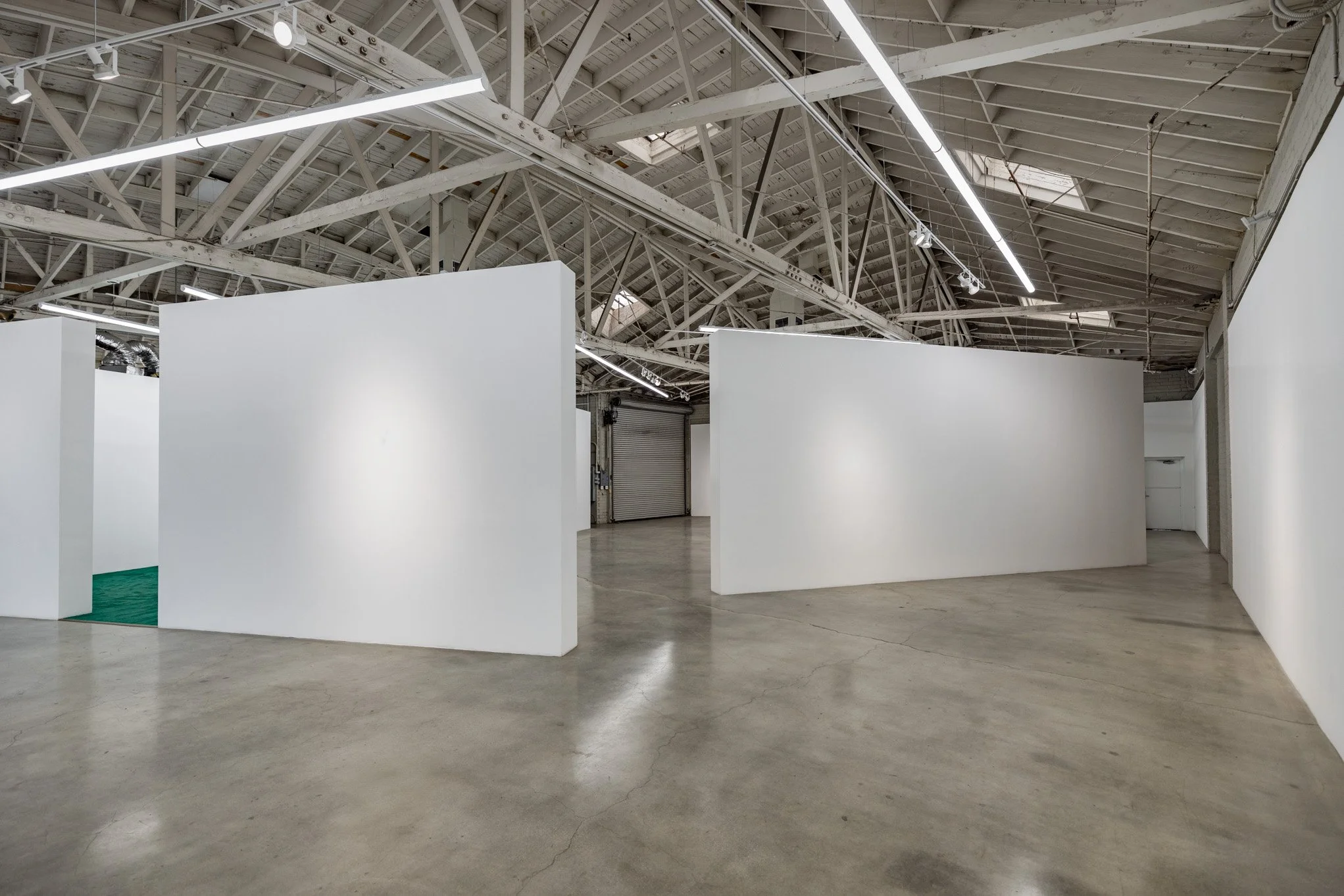 An empty art gallery with white walls and an industrial ceiling with exposed beams and lighting fixtures.