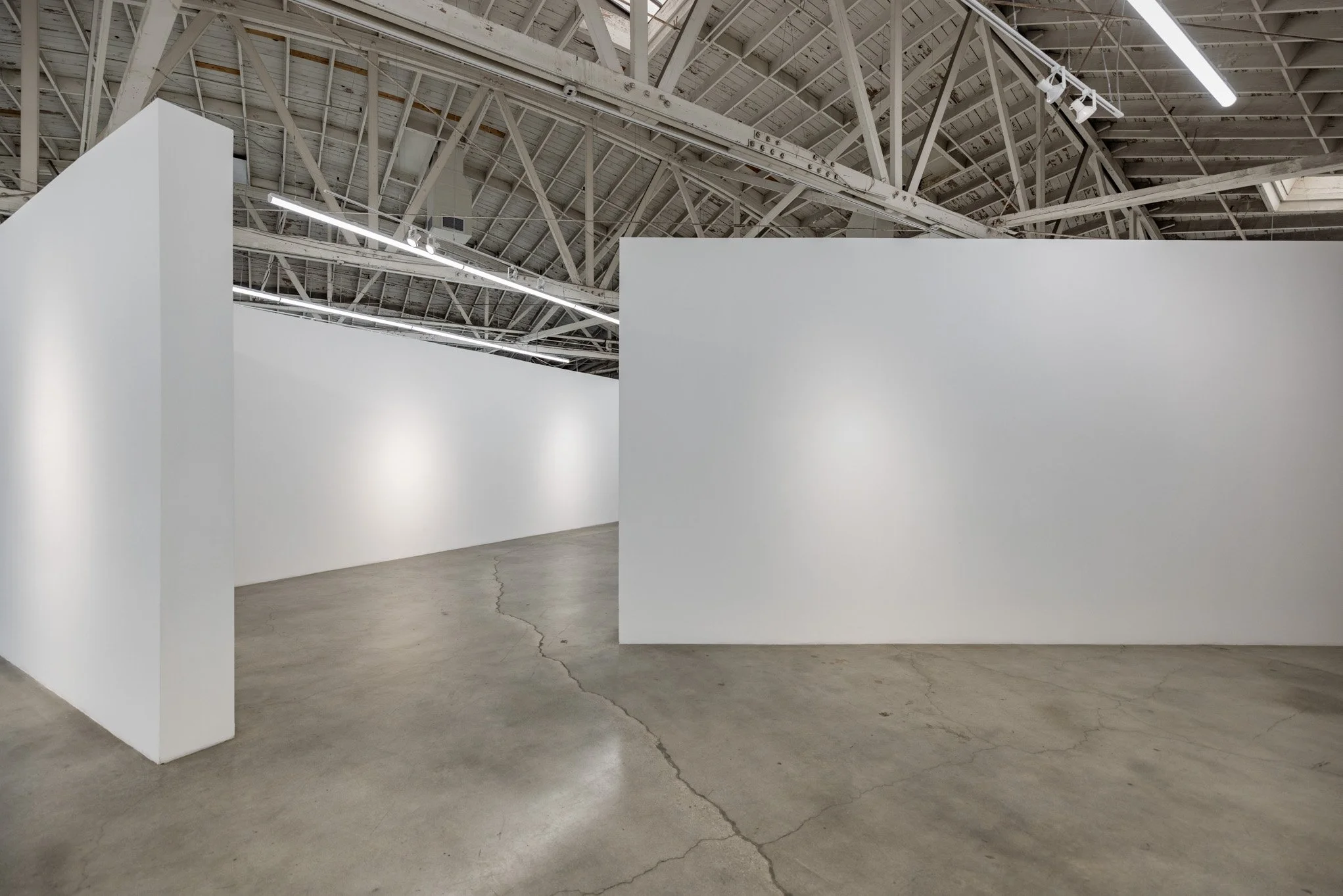 Empty white gallery walls in an industrial-style art museum or gallery space with a cracked concrete floor