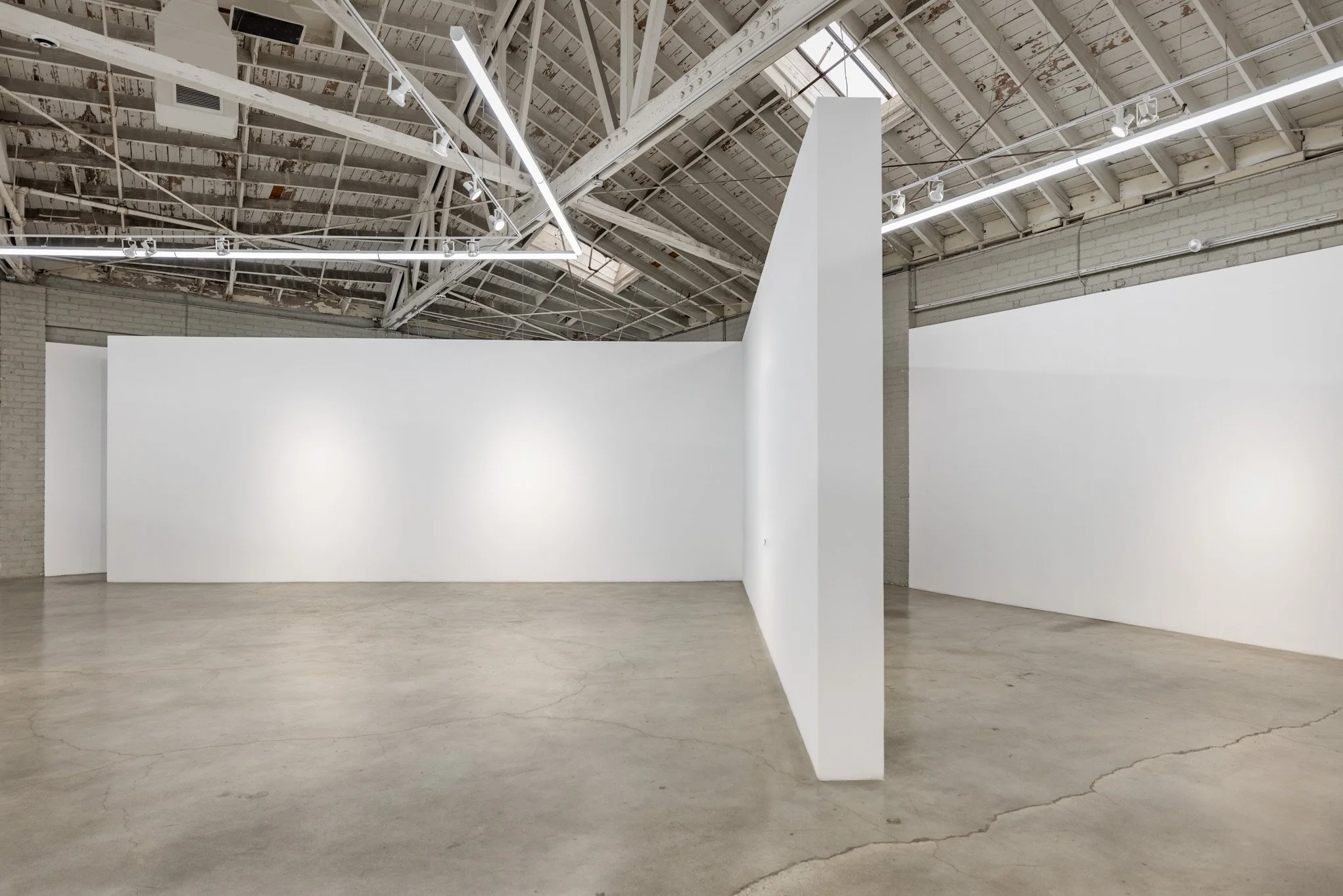 Empty art gallery with white walls and concrete floor, industrial ceiling with metal beams and exposed ductwork, modern lighting fixtures