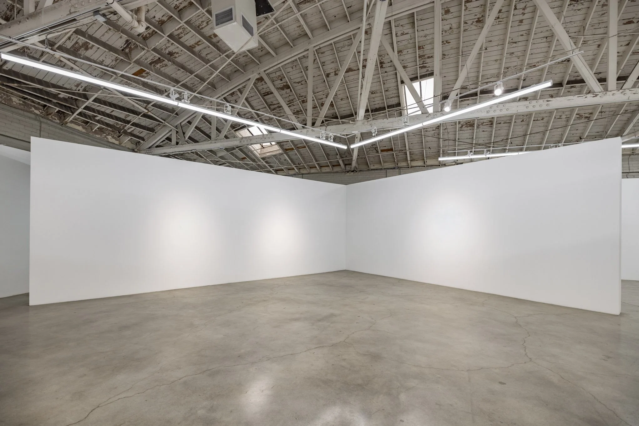 Empty white gallery walls in an industrial art gallery space with exposed ceiling and concrete floor.