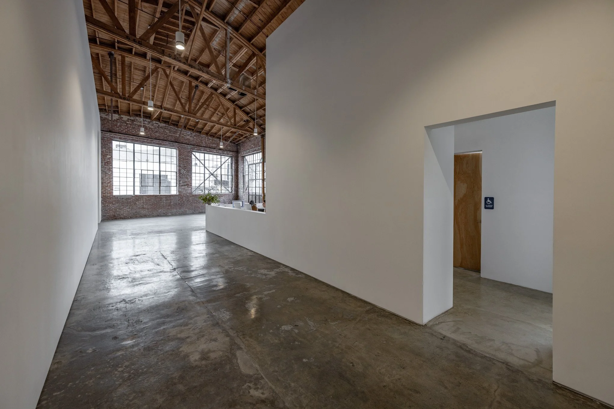 Modern industrial-style interior with exposed brick walls, large multi-pane windows, a wooden vaulted ceiling, and polished concrete floors.