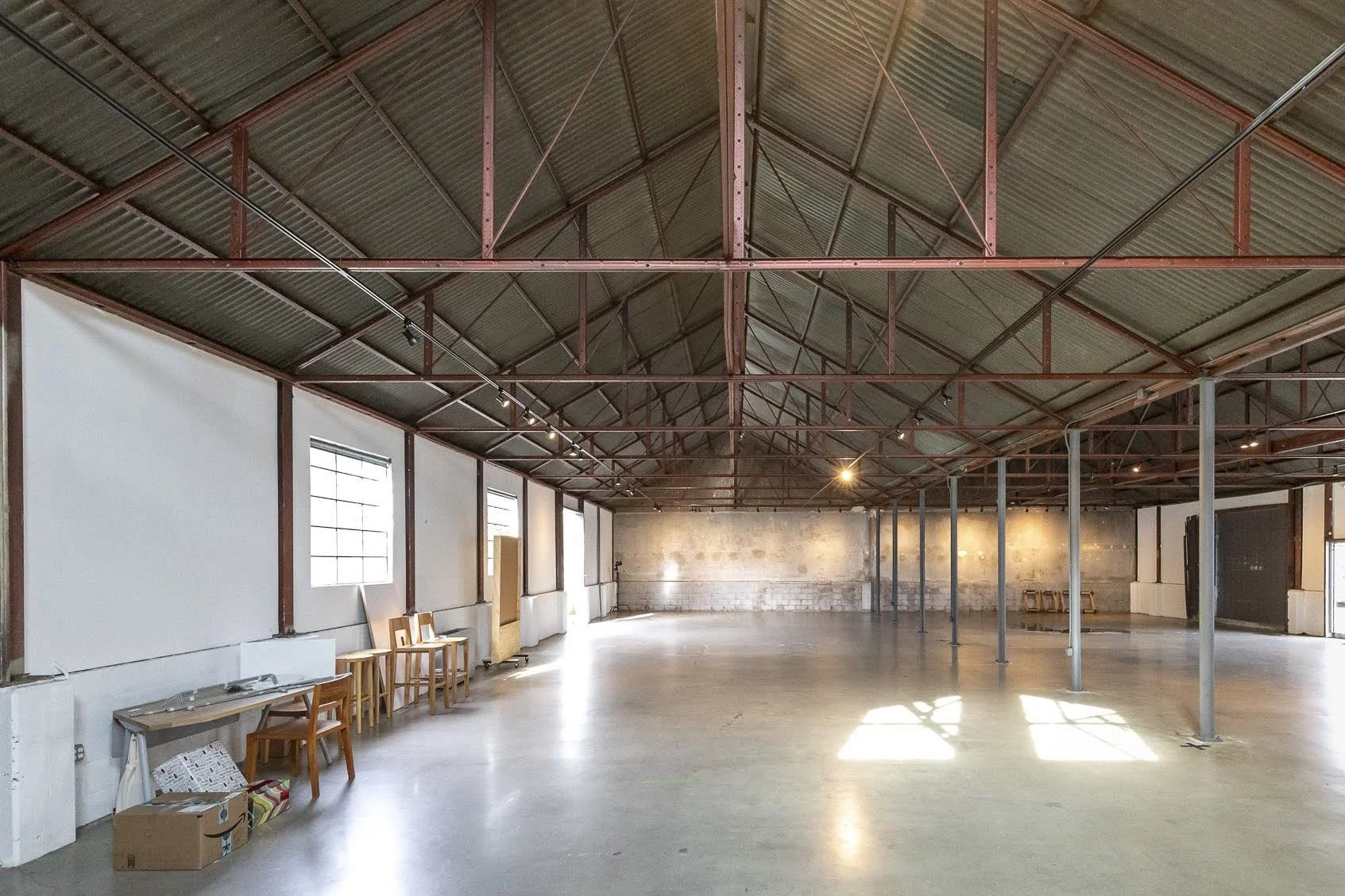 Empty industrial warehouse with exposed metal beams and concrete floor, sunlight streaming through windows.