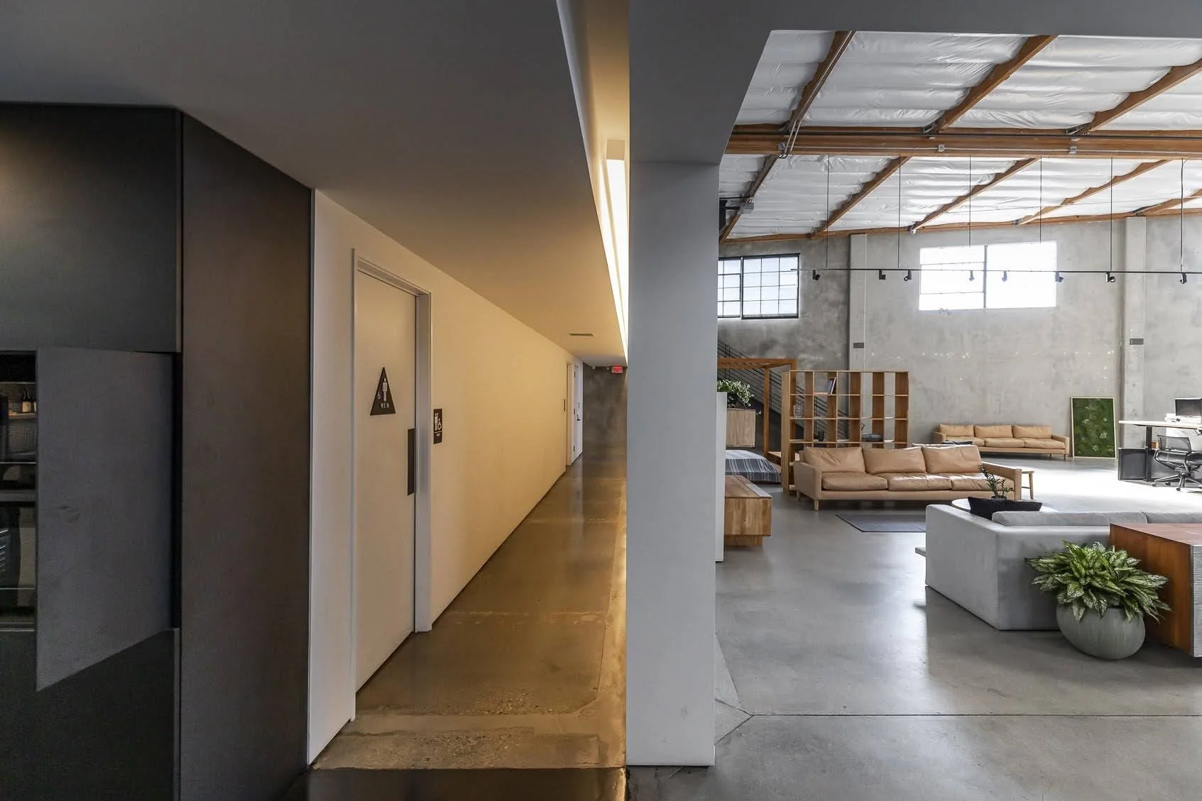 Interior view of a modern, industrial-style lounge with seating areas, large windows, and exposed ceiling beams.