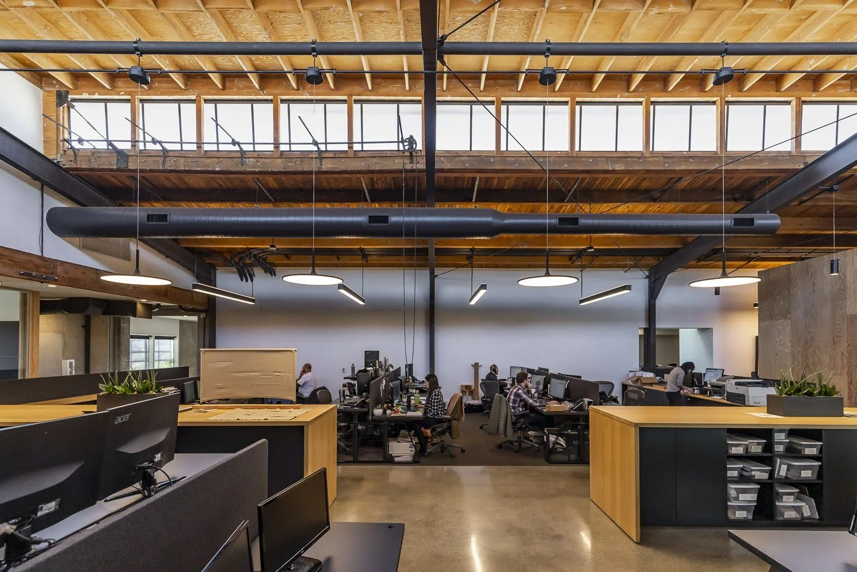 Open-plan office with workstations, employees working at computers, wooden accents, and large windows allowing natural light.