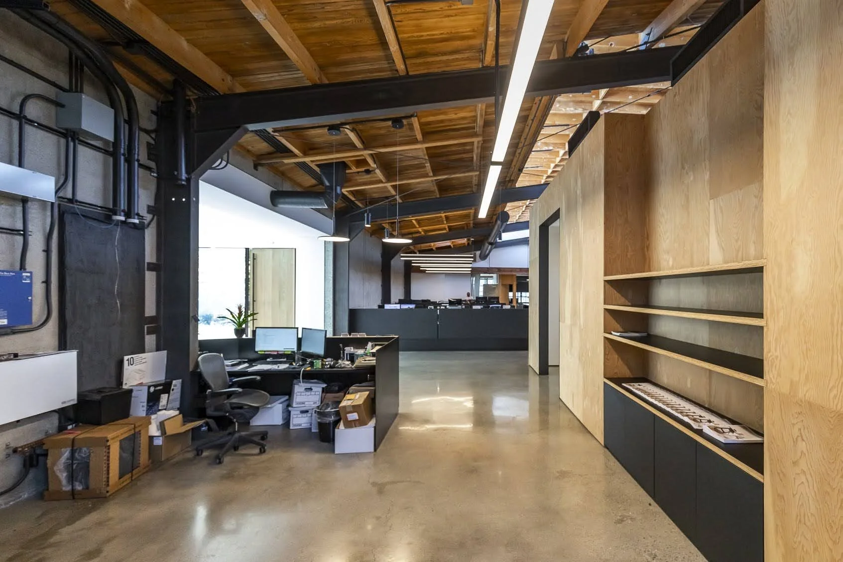 Modern office with desk, computer monitors, chair, and open shelving, featuring wooden and metal accents.