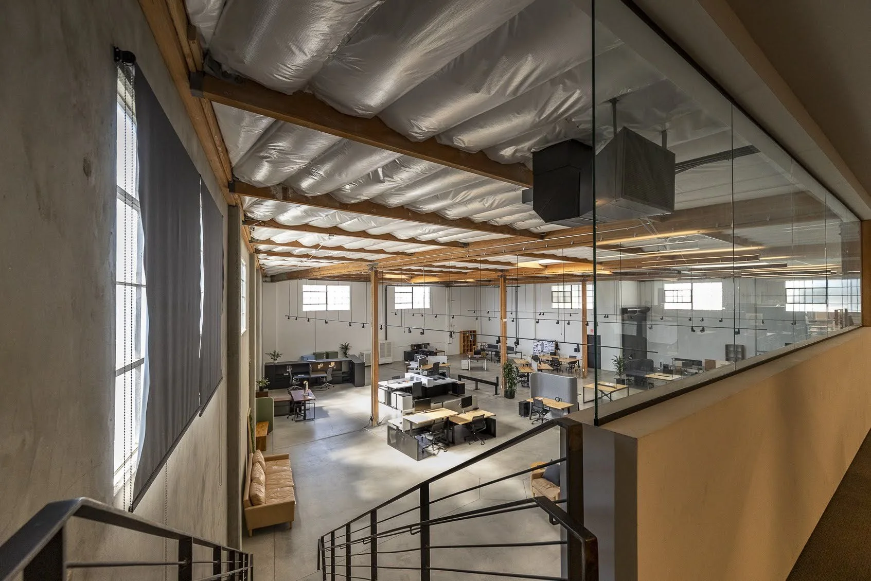 Interior view of a modern, open-plan Office space with large windows, multiple desks, chairs, plants, and a glass wall.