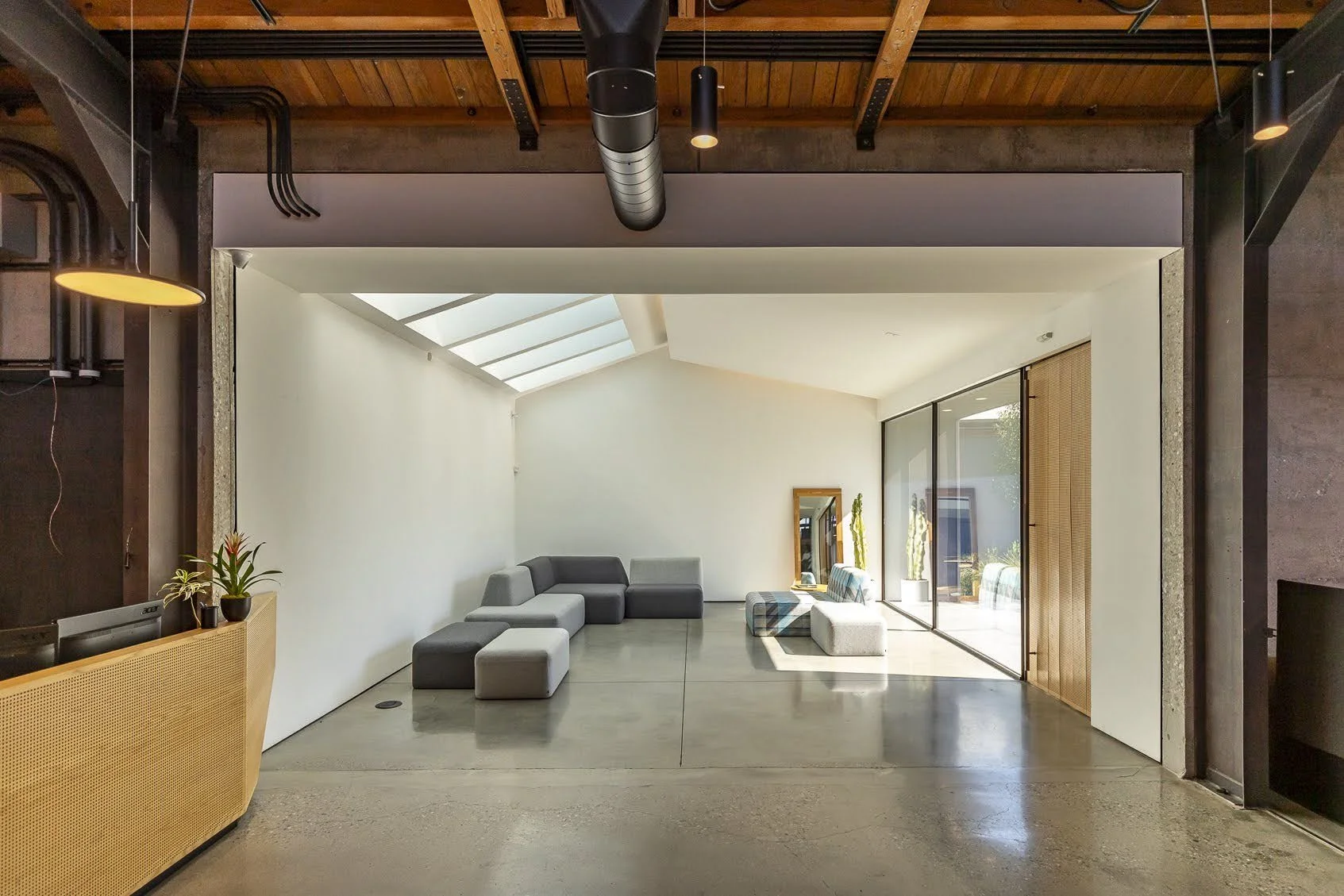 Modern living room with gray sectional sofa, abstract ottomans, large glass sliding doors, natural light and wooden ceiling.