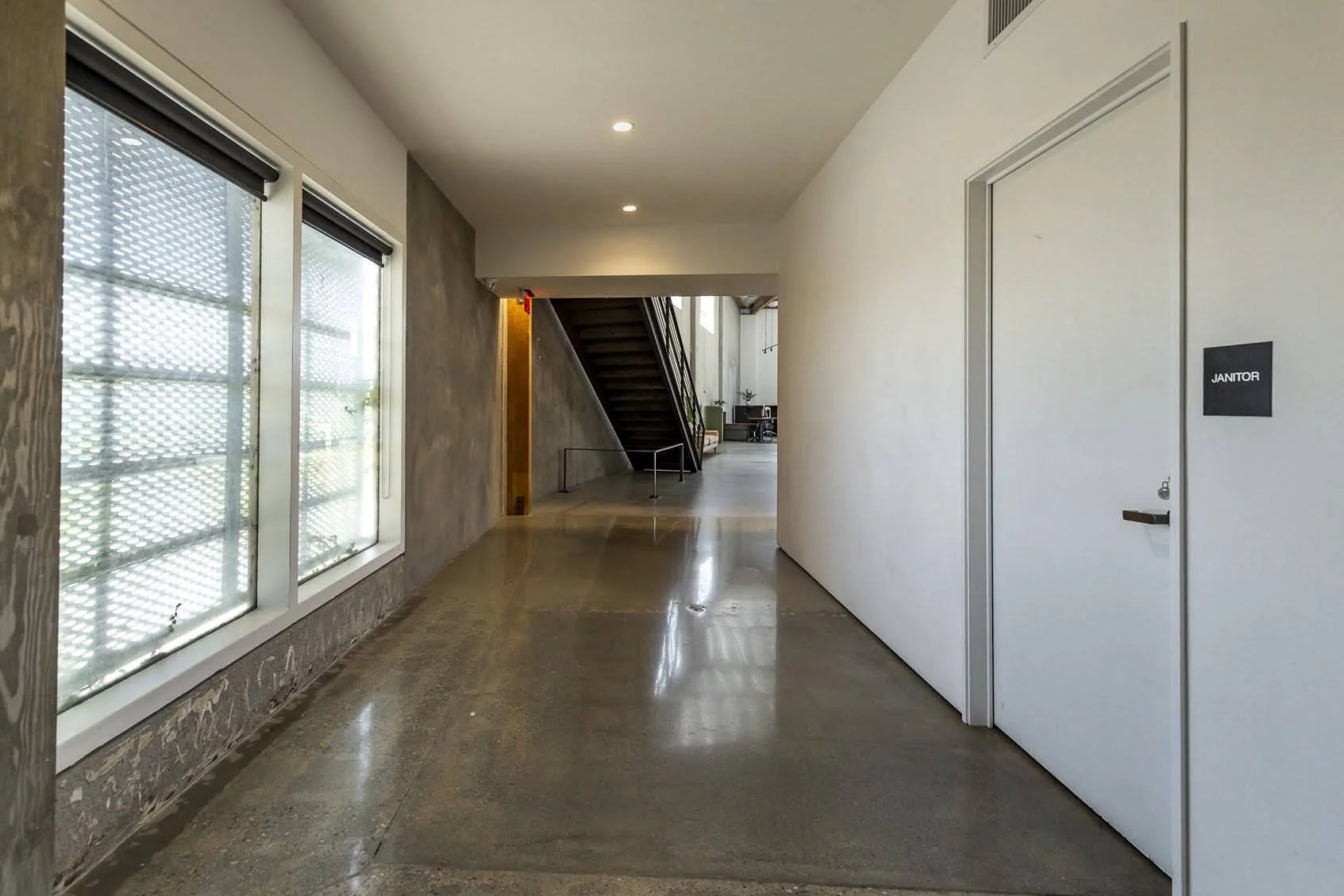 Interior hallway with windows on the left, a staircase at the end, and a door labeled 'Janitor' on the right.