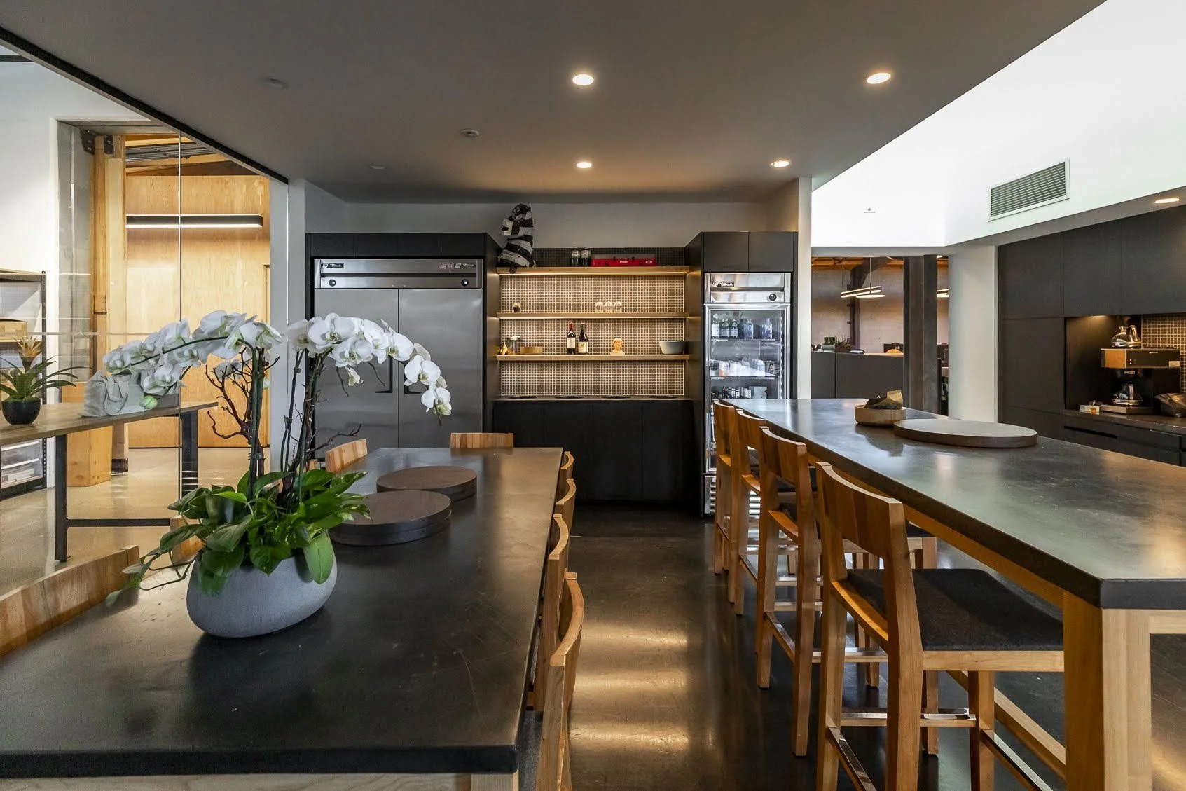 Modern kitchen with black countertops, wooden chairs, and a flower vase with white orchids on the table.