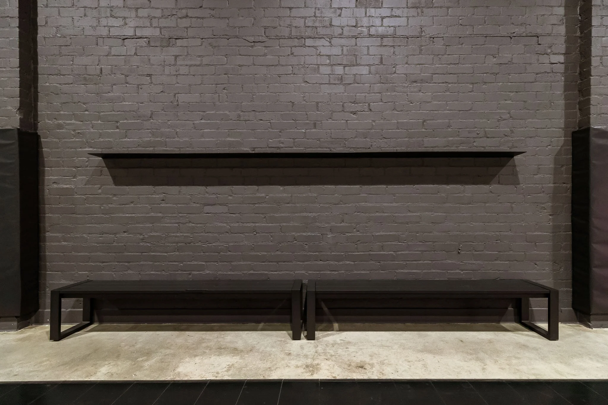 Empty black bench and shelf against a gray brick wall in a modern interior.