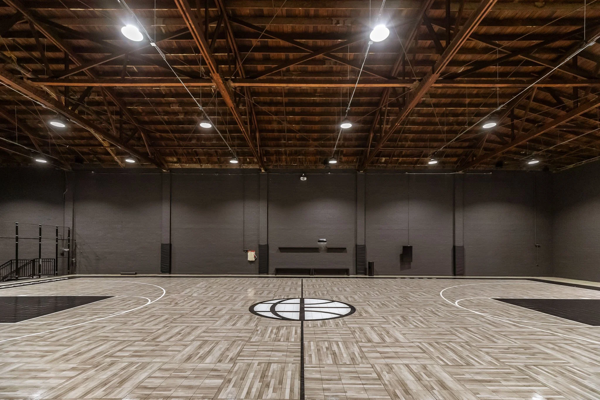 Empty indoor basketball court with hoop and black walls.