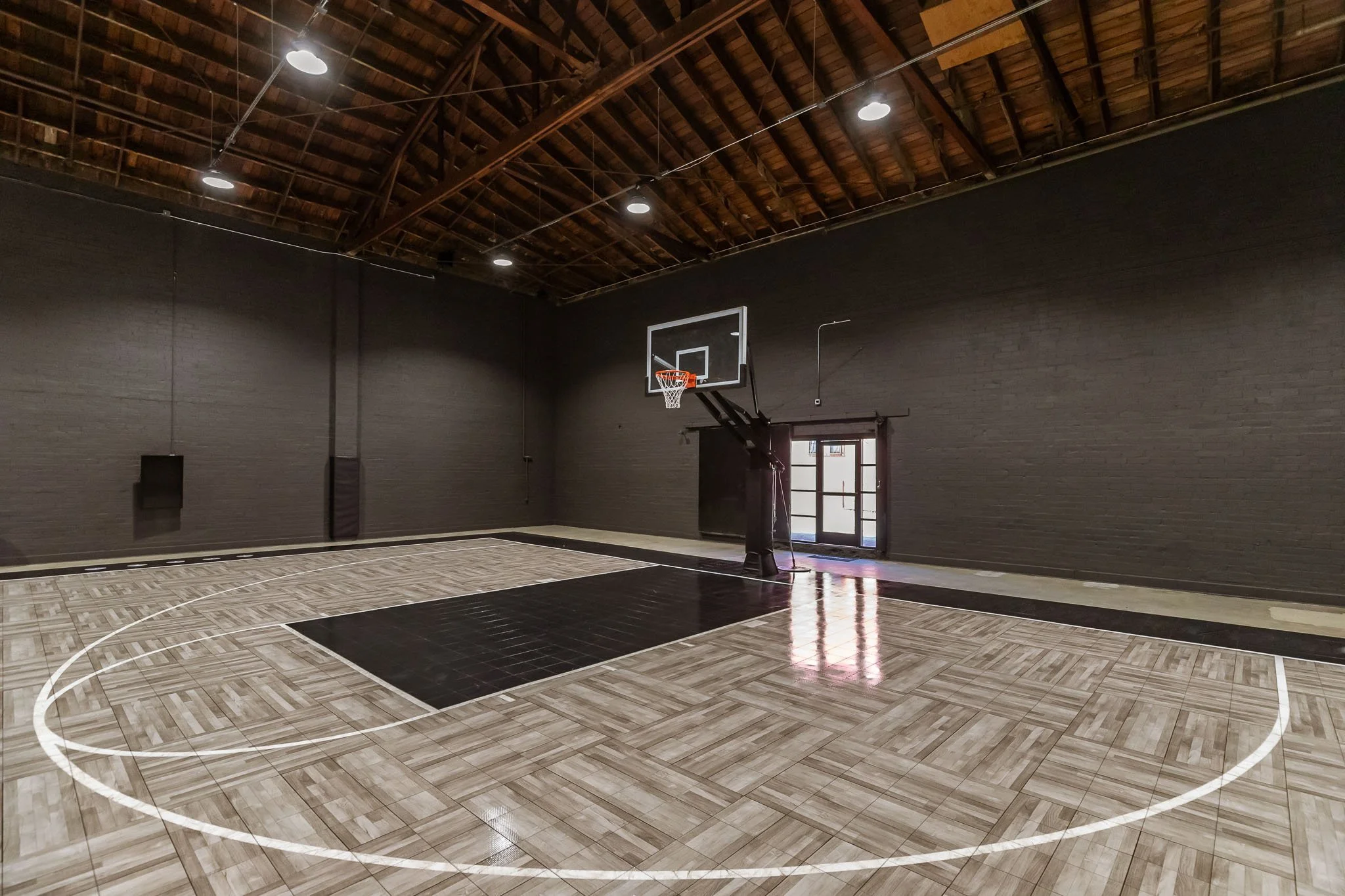 Indoor basketball court with a black wall, a hoop, and a wooden floor.