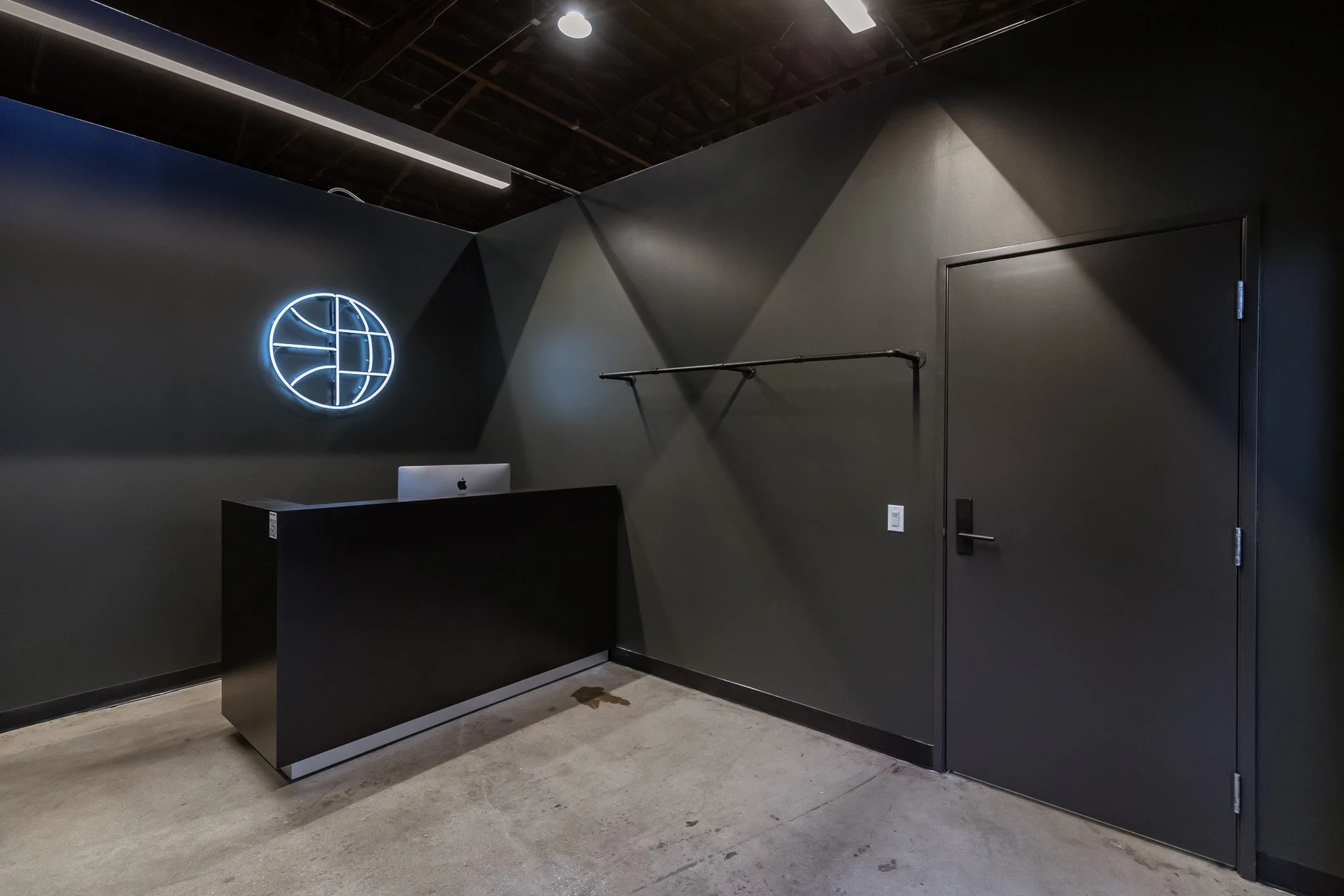 Modern black reception counter with a neon globe logo on a dark gray wall, a black door, and a minimalist clothing rack inside a sleek, industrial-style interior.