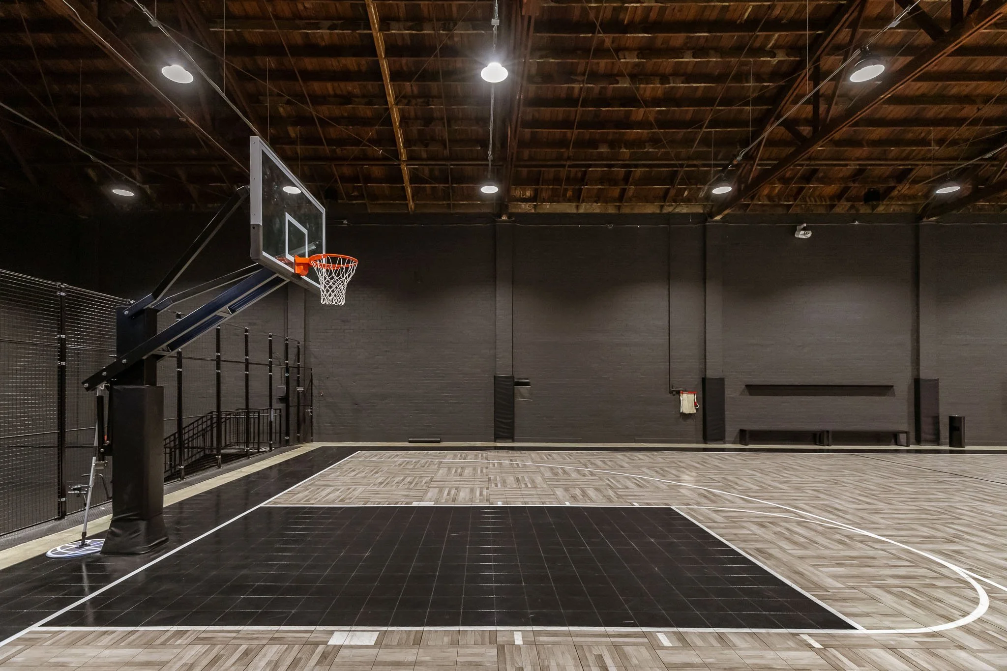 Empty indoor basketball court with a hoop, black walls, and wooden ceiling.