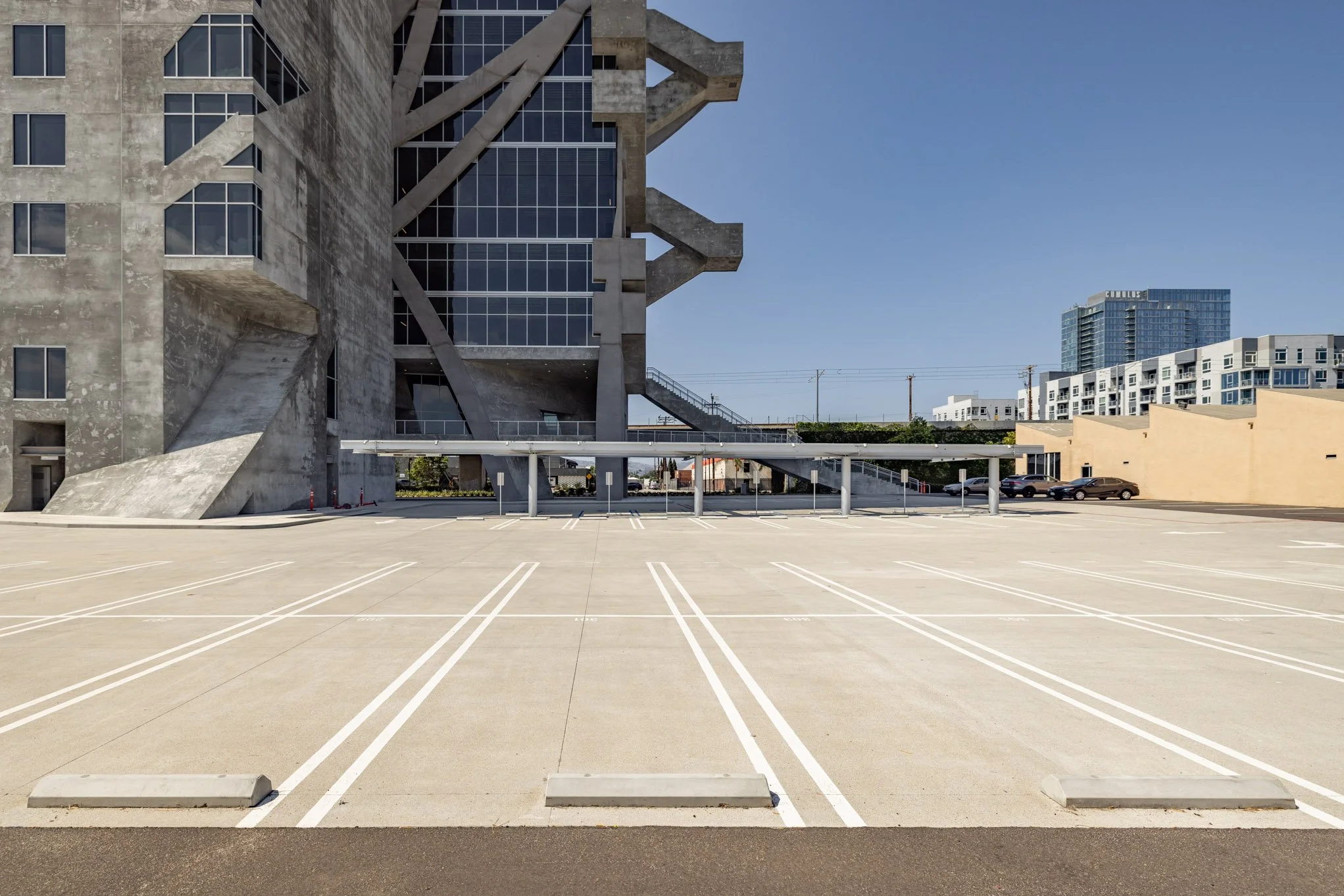 Empty parking lot with a large modern building in the background under a clear blue sky.