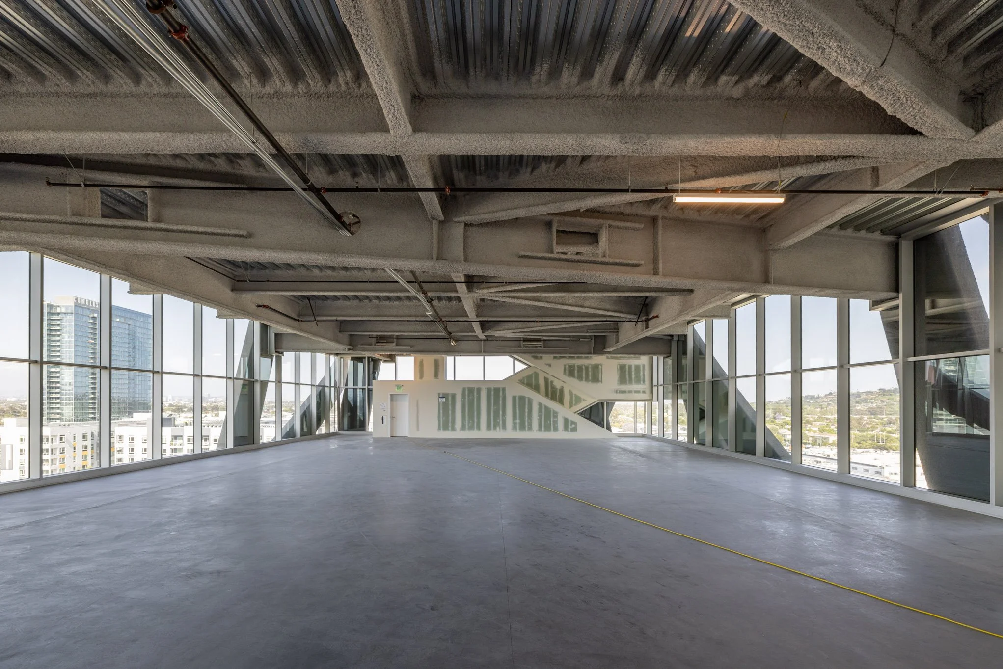 Empty modern office space with large windows, exposed ceiling, and a polished concrete floor.
