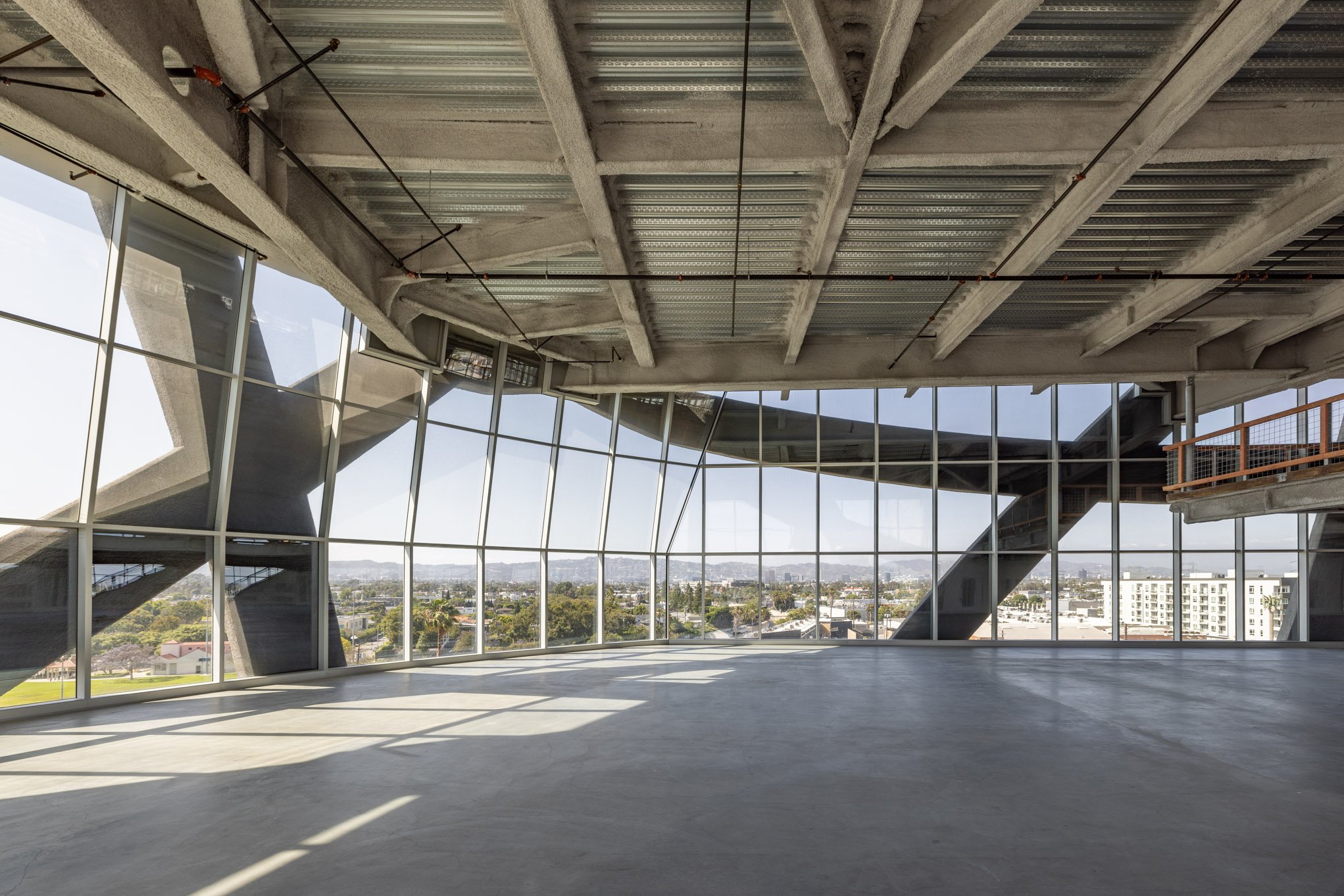 Empty modern interior space with large glass windows and unfinished ceiling, overlooking a cityscape.