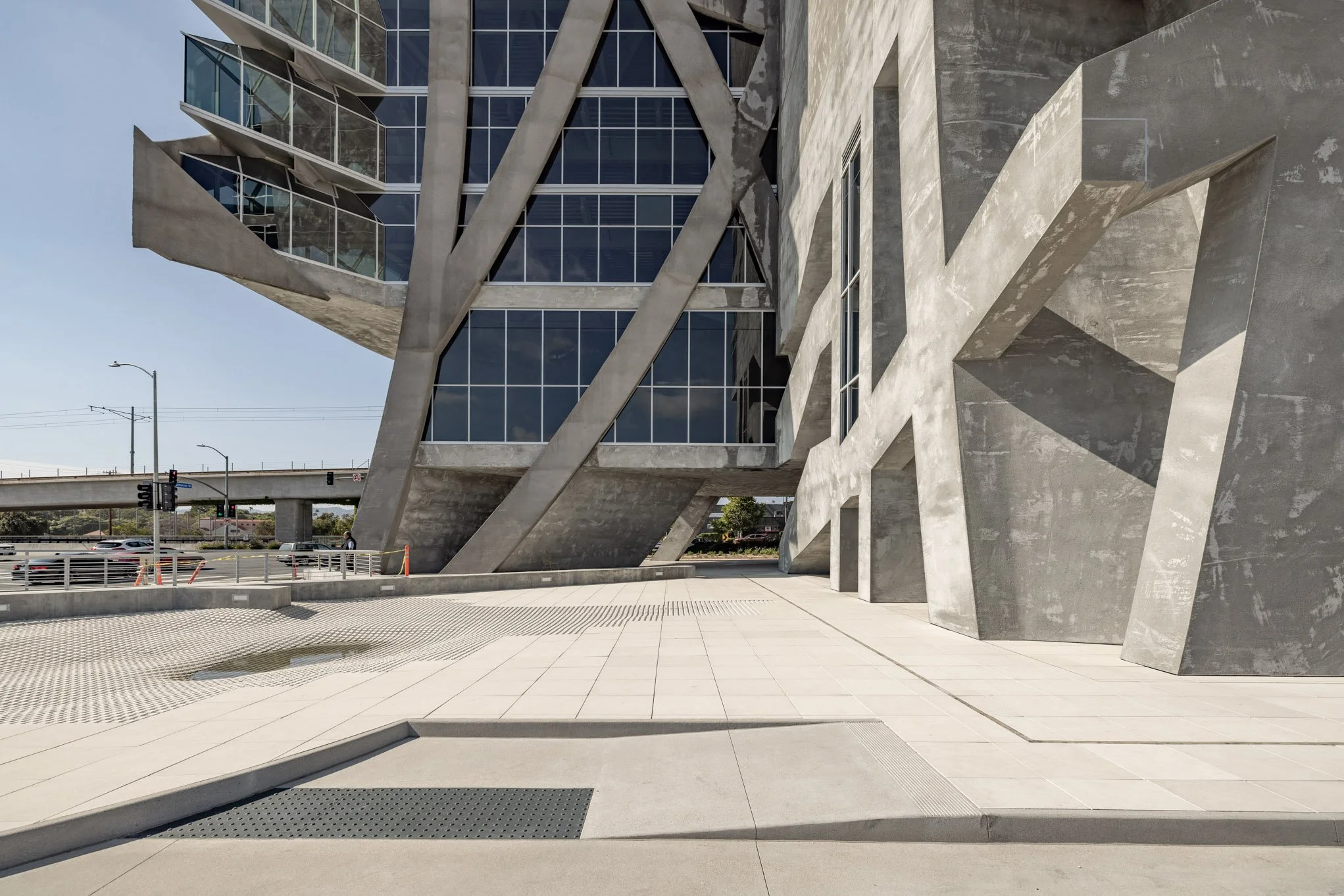 Modern building with angular concrete and glass design, featuring large windows and geometric shapes, located on a city street with traffic and lampposts.