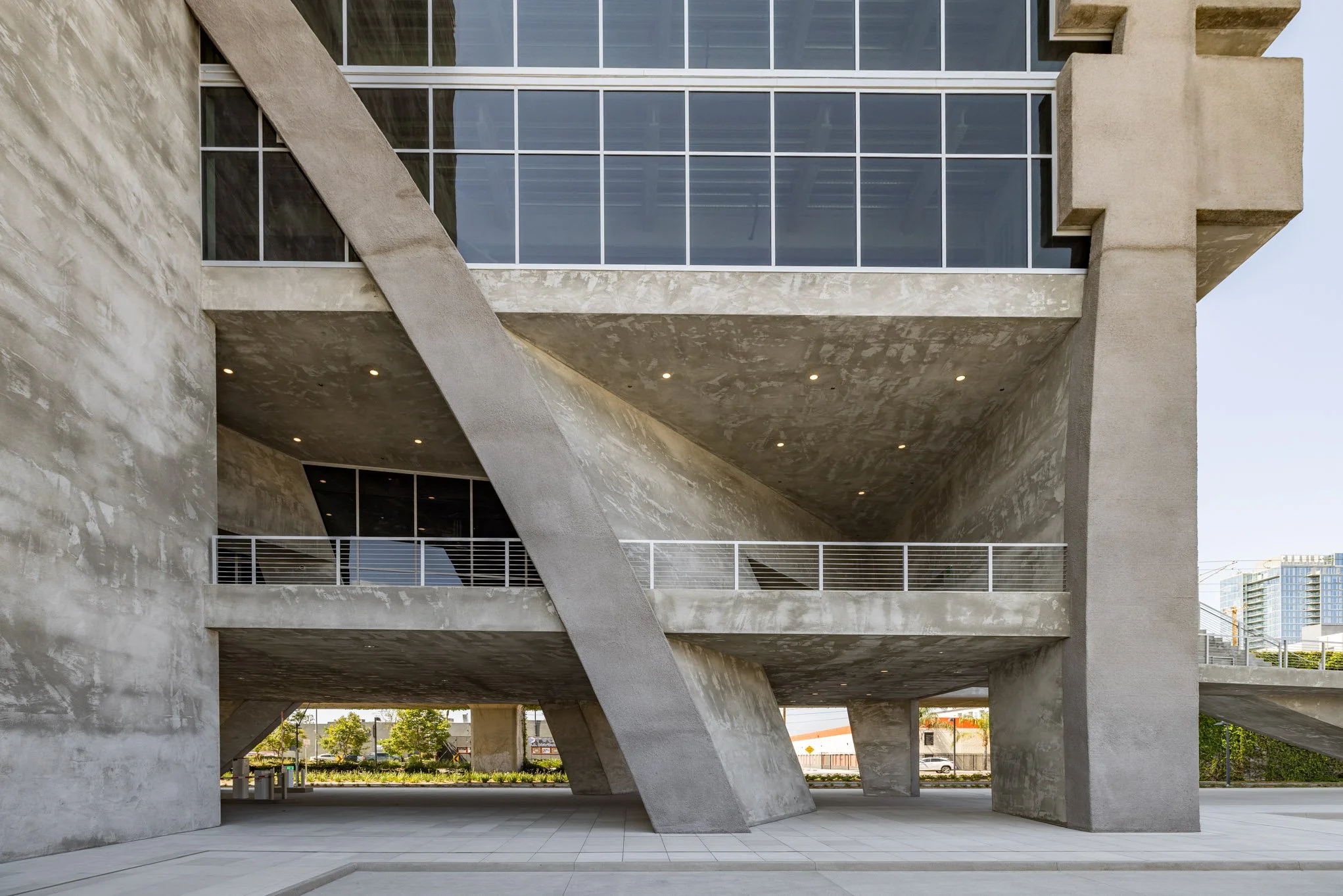 Modern concrete building with angular design, multiple levels, and large glass windows, with a paved sidewalk in the foreground.