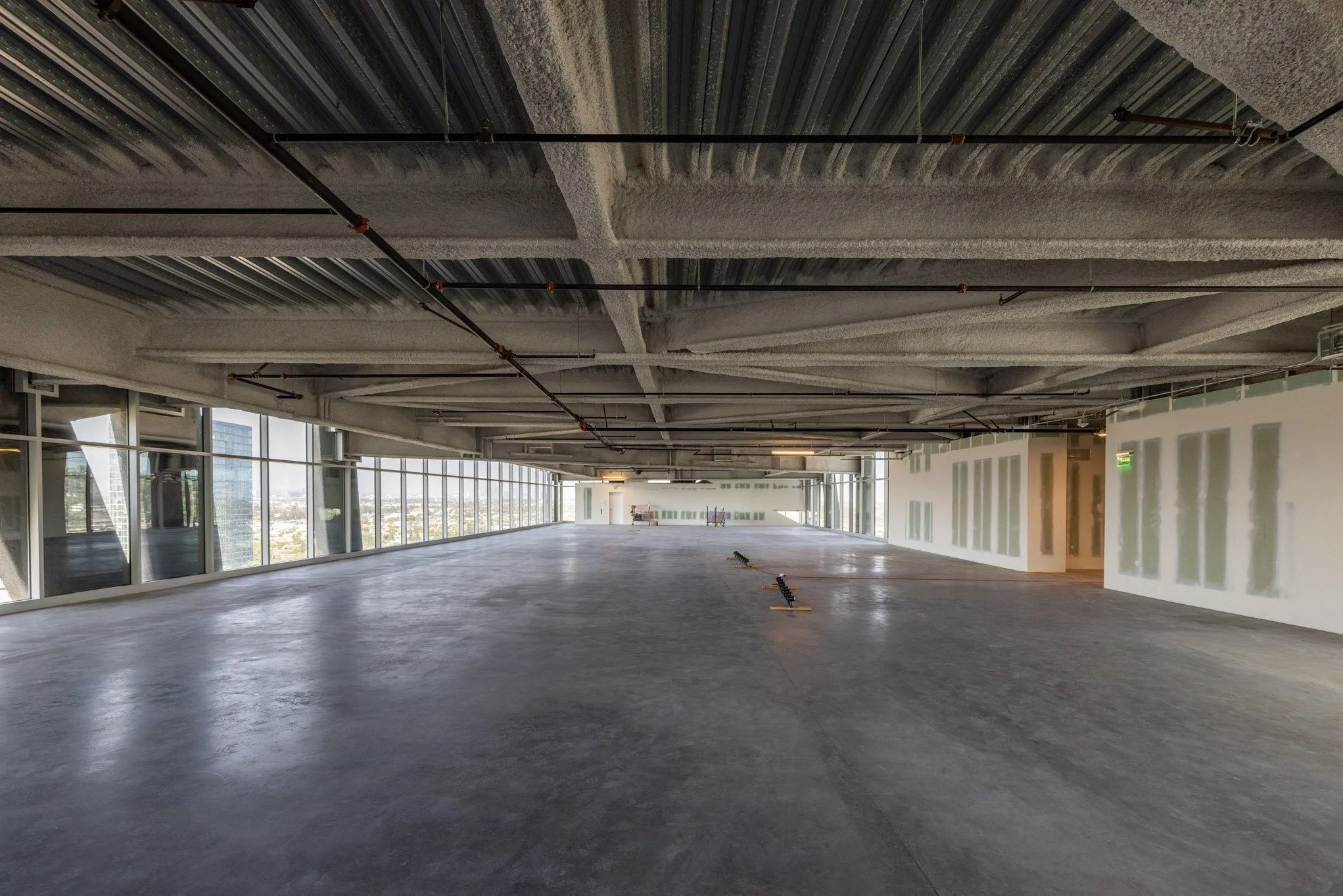 Empty interior space with large windows, unfinished walls, and concrete floor, likely under construction or renovation.