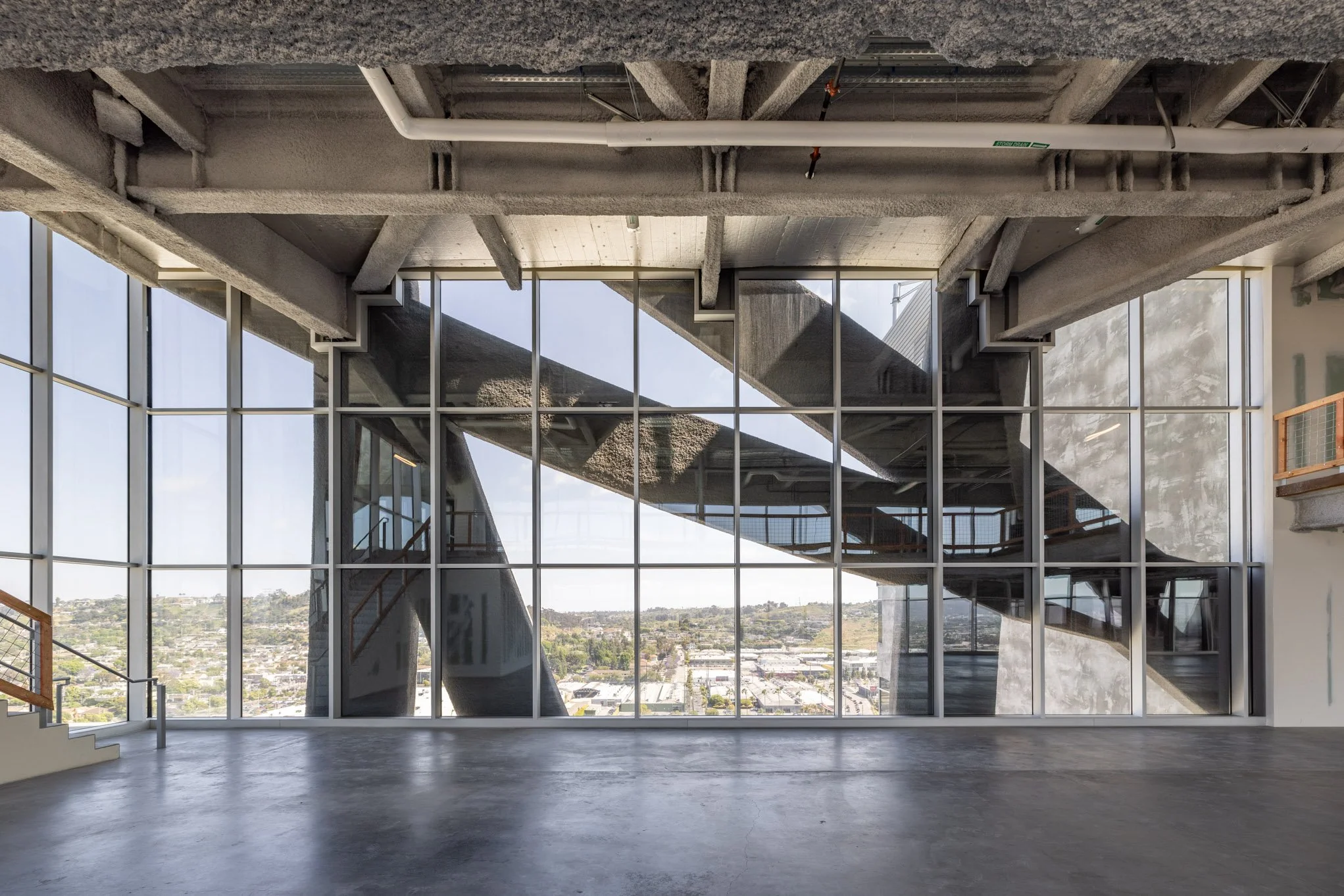 Interior of a modern building with large glass windows showing a cityscape and an unusual, abstract concrete structure outside the window.