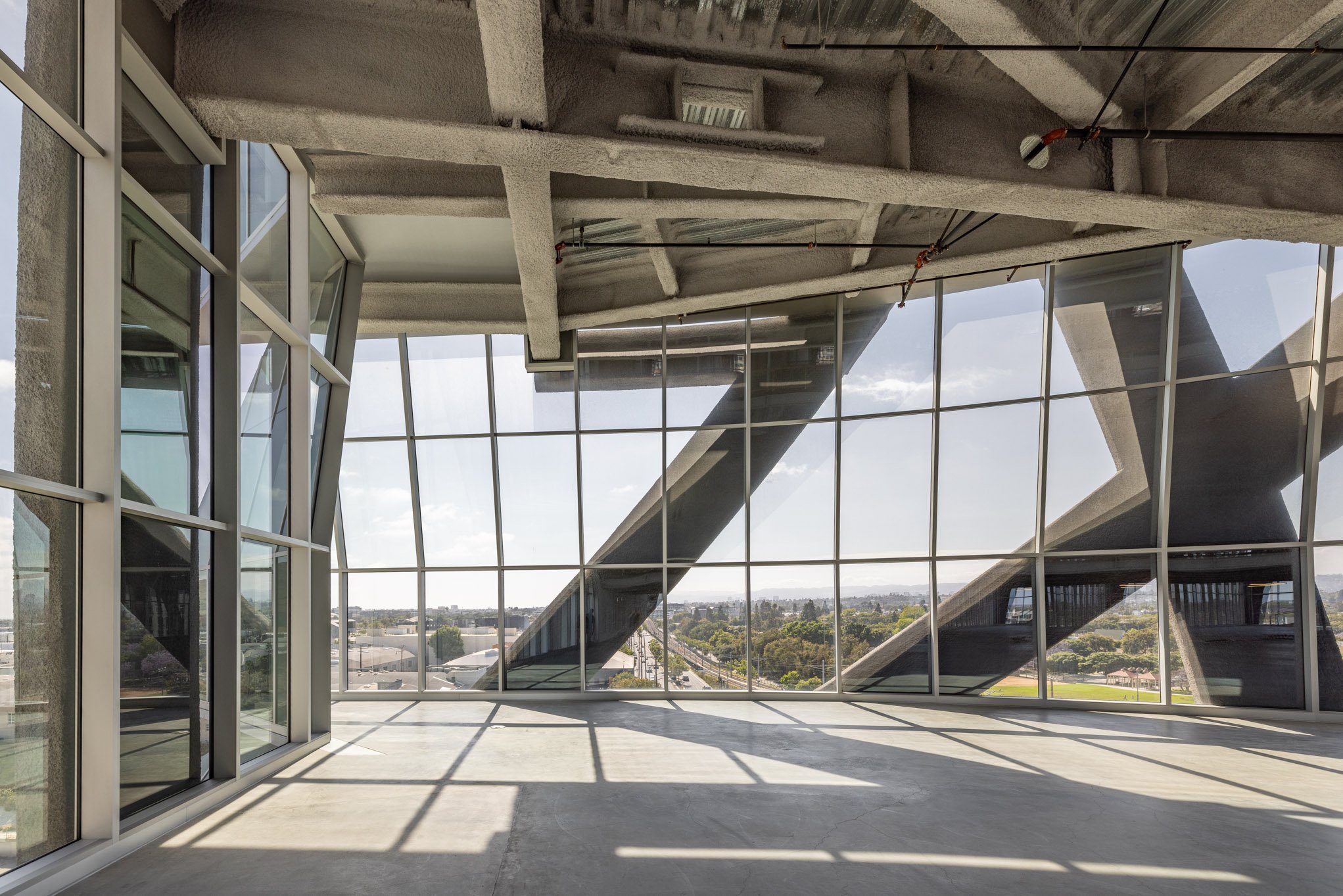Interior view of a modern building with large glass windows, concrete structure, and a view of the cityscape outside.