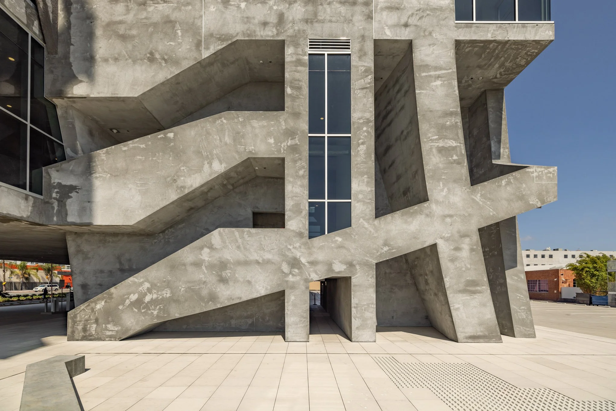 Modern concrete building with geometric design, featuring large angular shapes and a tall vertical window, set against a blue sky.