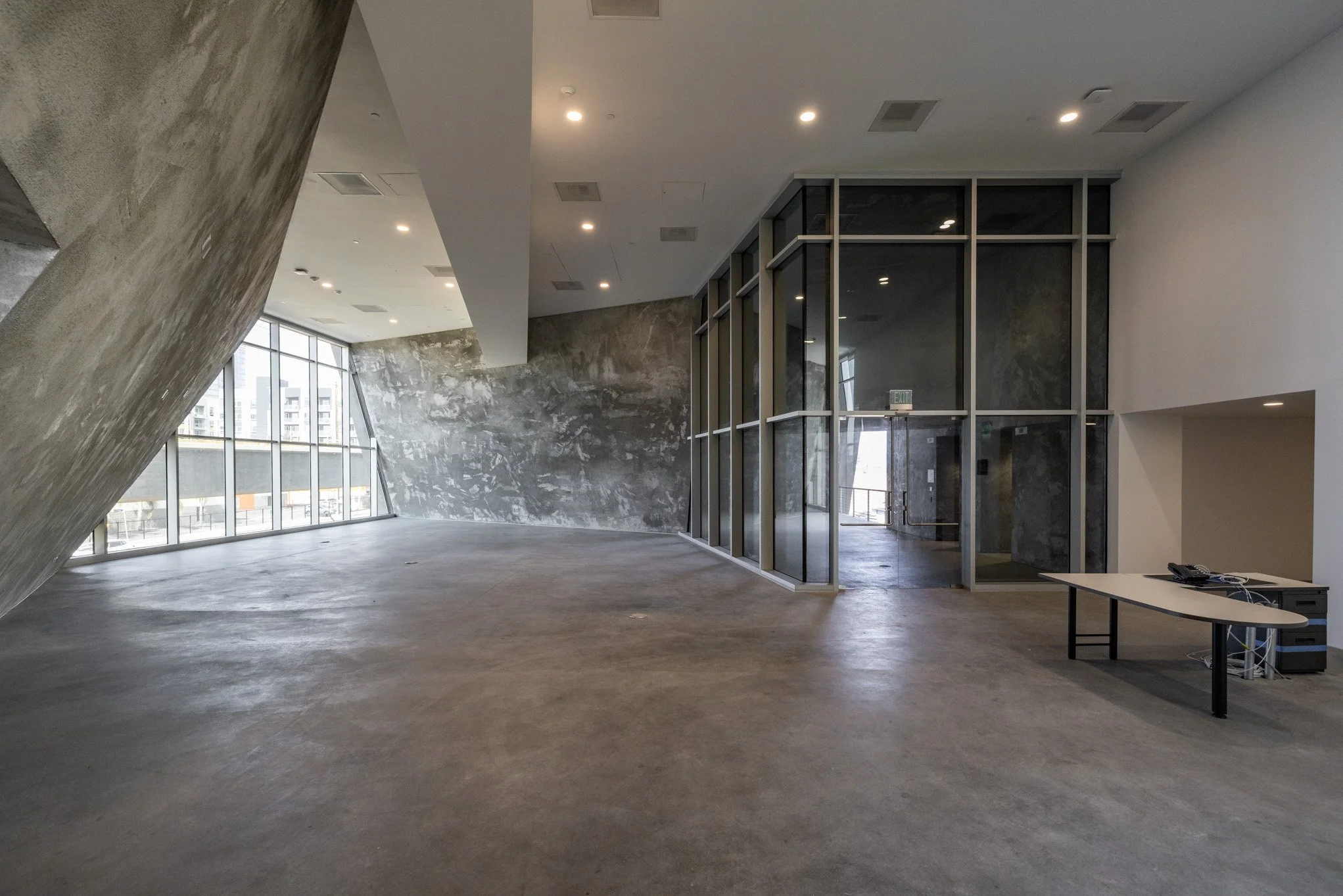 Empty modern office space with concrete floors, large windows, and glass partition walls.