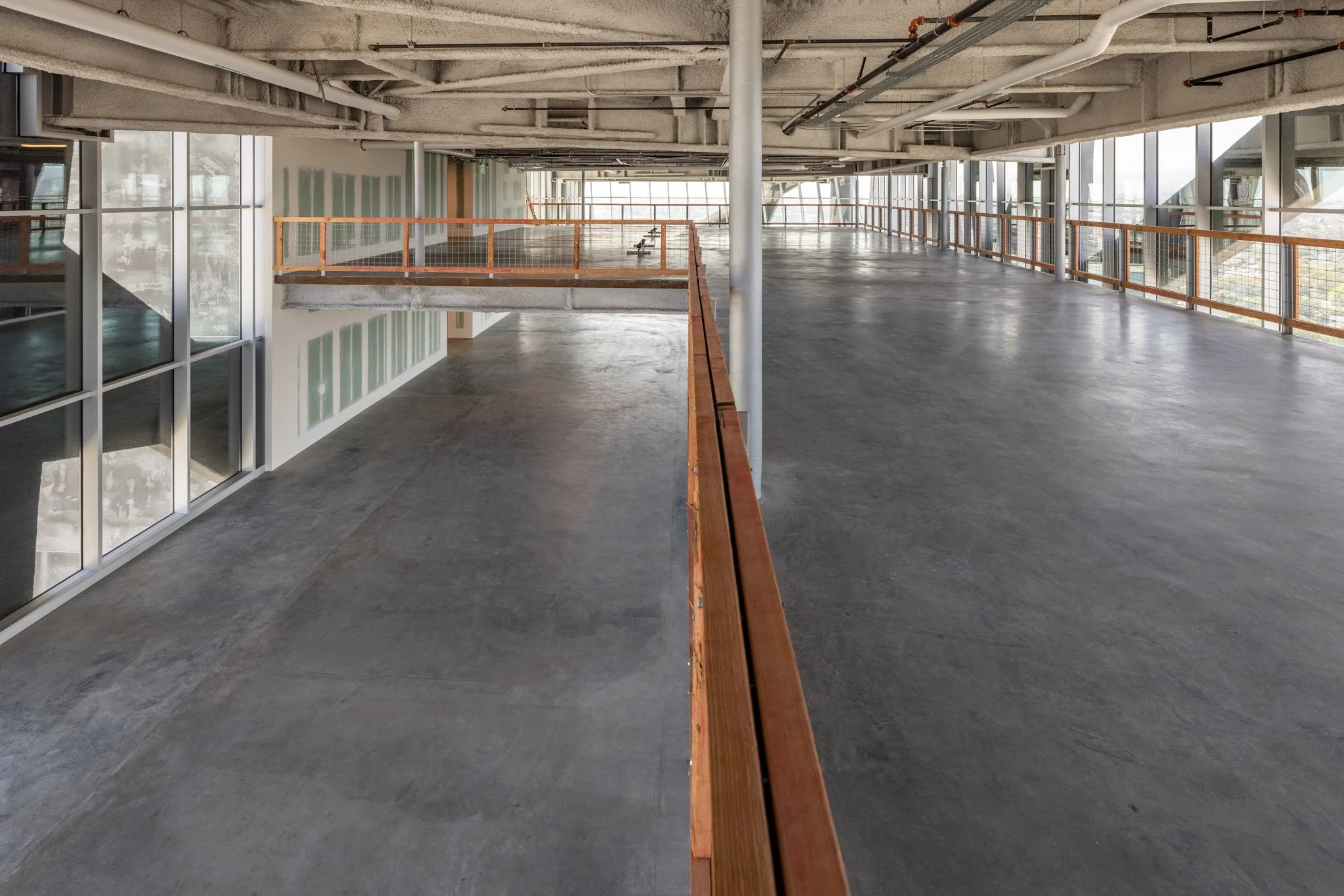 Empty multi-level parking garage with concrete floors, orange safety railings, and large glass windows letting in natural light.
