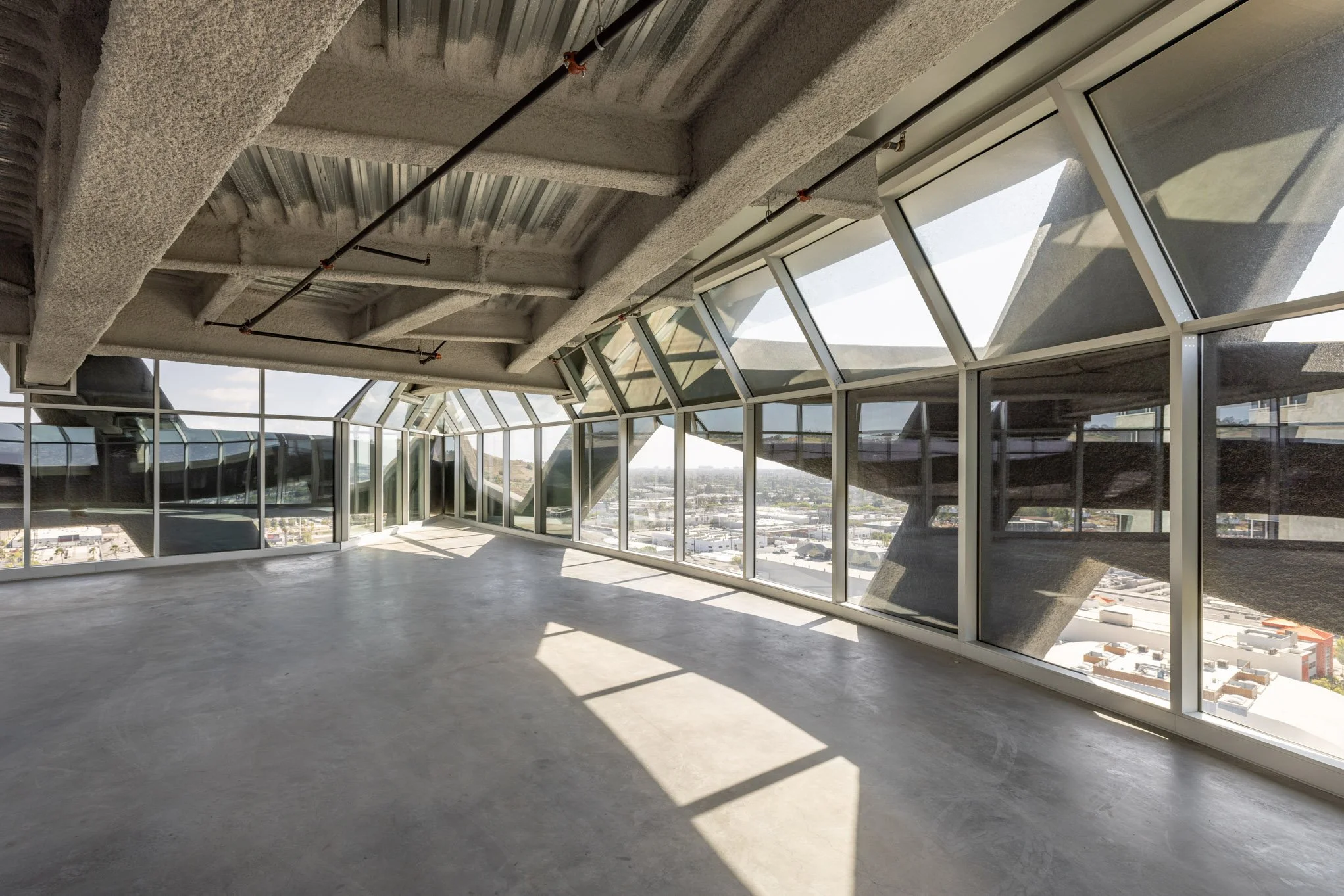 Empty modern office space with large glass windows, concrete floor, and exposure of building's structural elements.