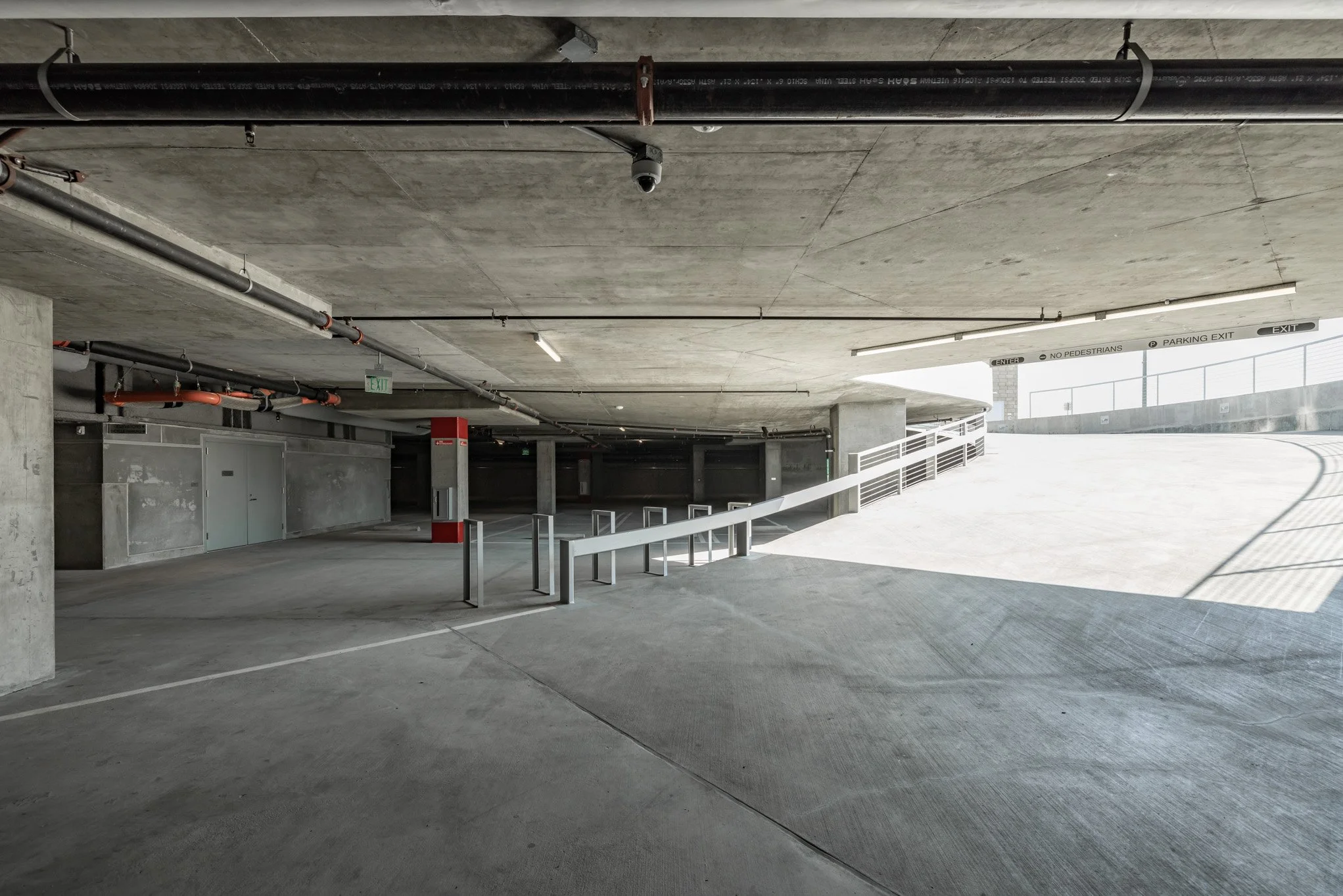 Empty multi-level parking garage with concrete walls, ceiling, and floor, featuring bike racks and signage for parking exit and pedestrian rules.