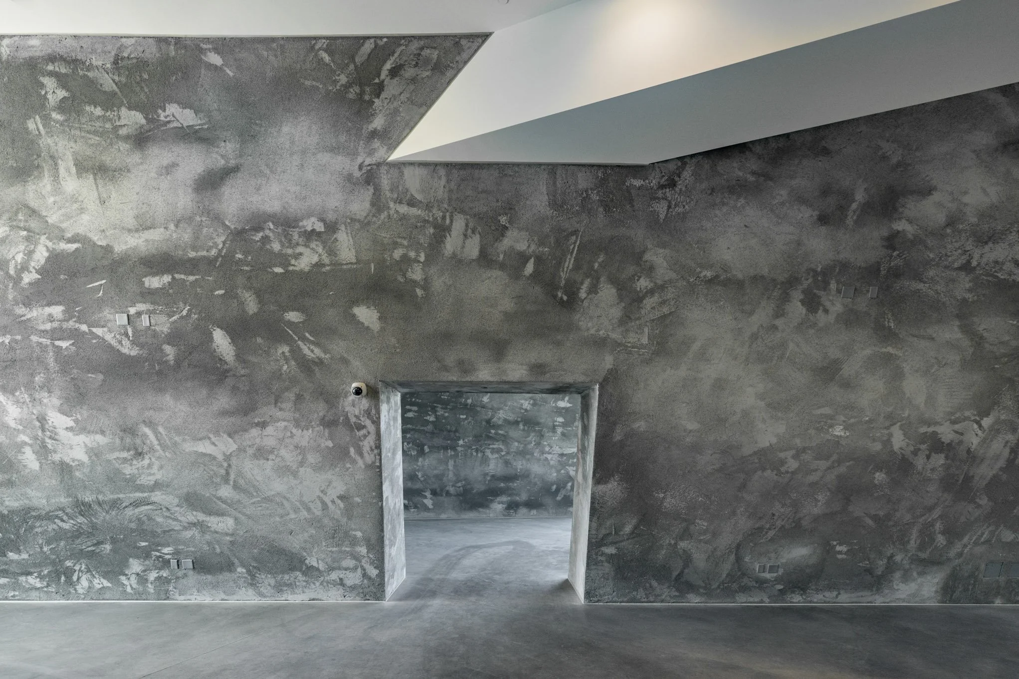 Interior view of a room with unfinished gray concrete walls and a doorway leading to another concrete space.