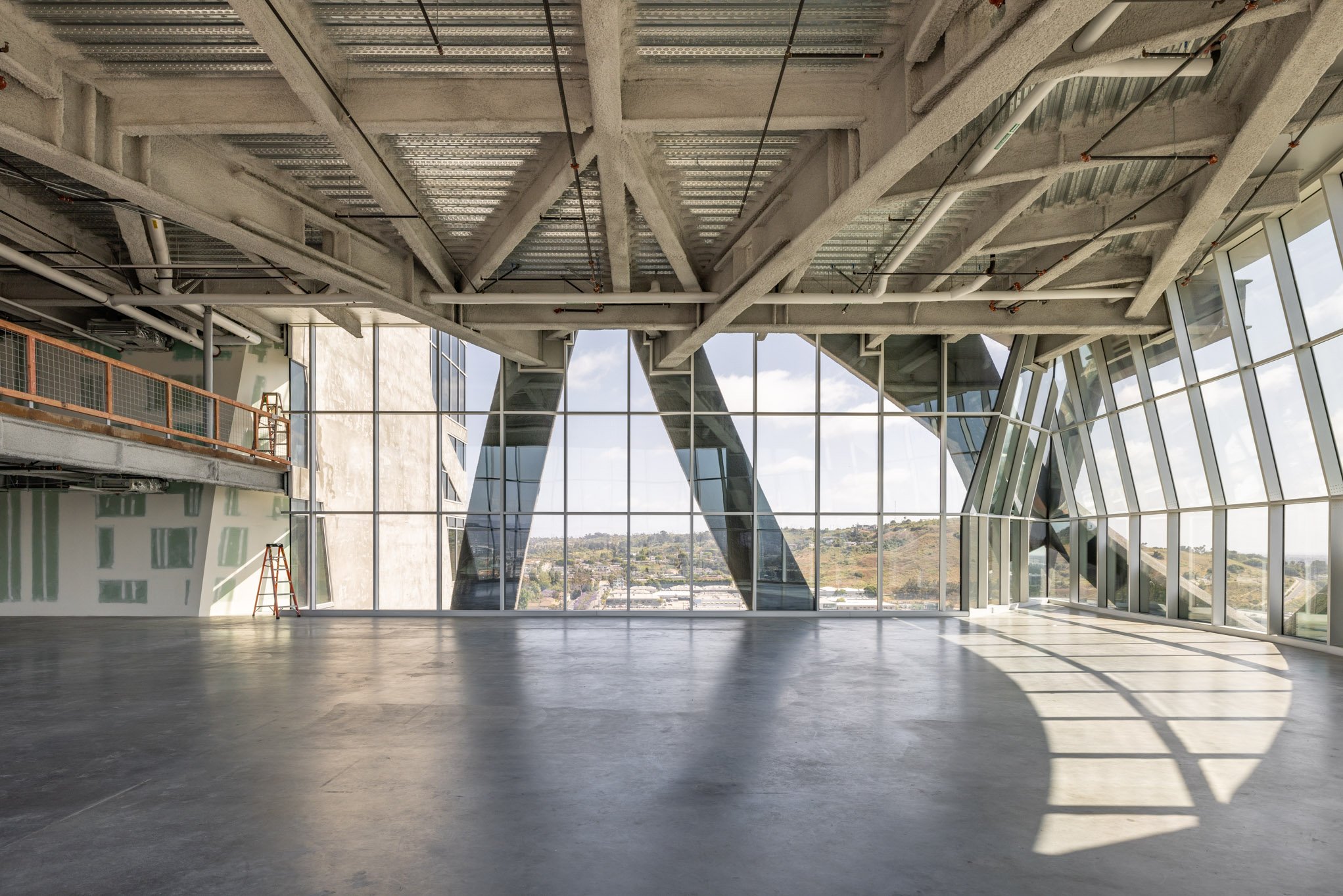 Empty modern building interior with large glass windows, concrete ceiling, and view of landscape outside.