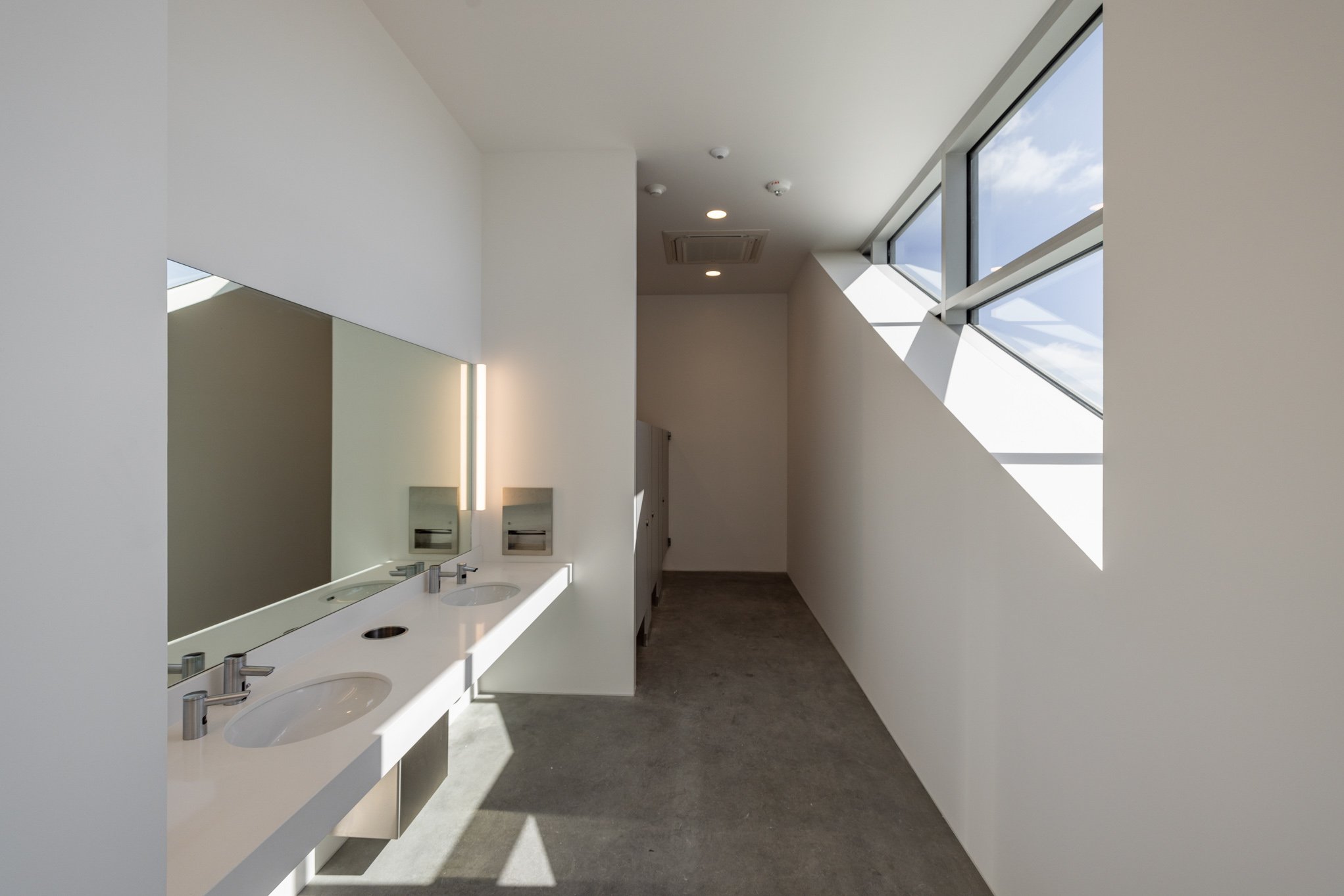 Empty men's restroom with two sinks, a large mirror, paper towel dispensers, and a window with natural light.