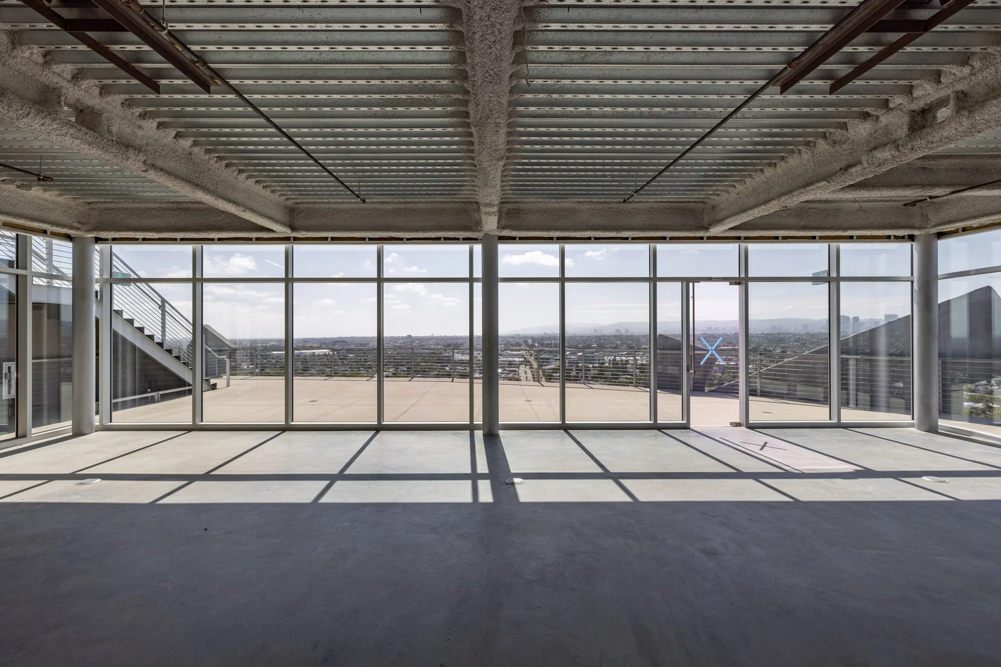 Empty room with large glass windows showing city skyline and blue sky with scattered clouds.