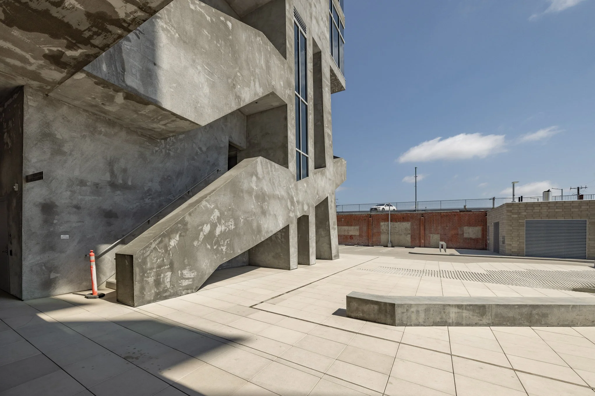 Empty outdoor concrete plaza with modern building and outdoor staircase, clear blue sky with a few clouds.